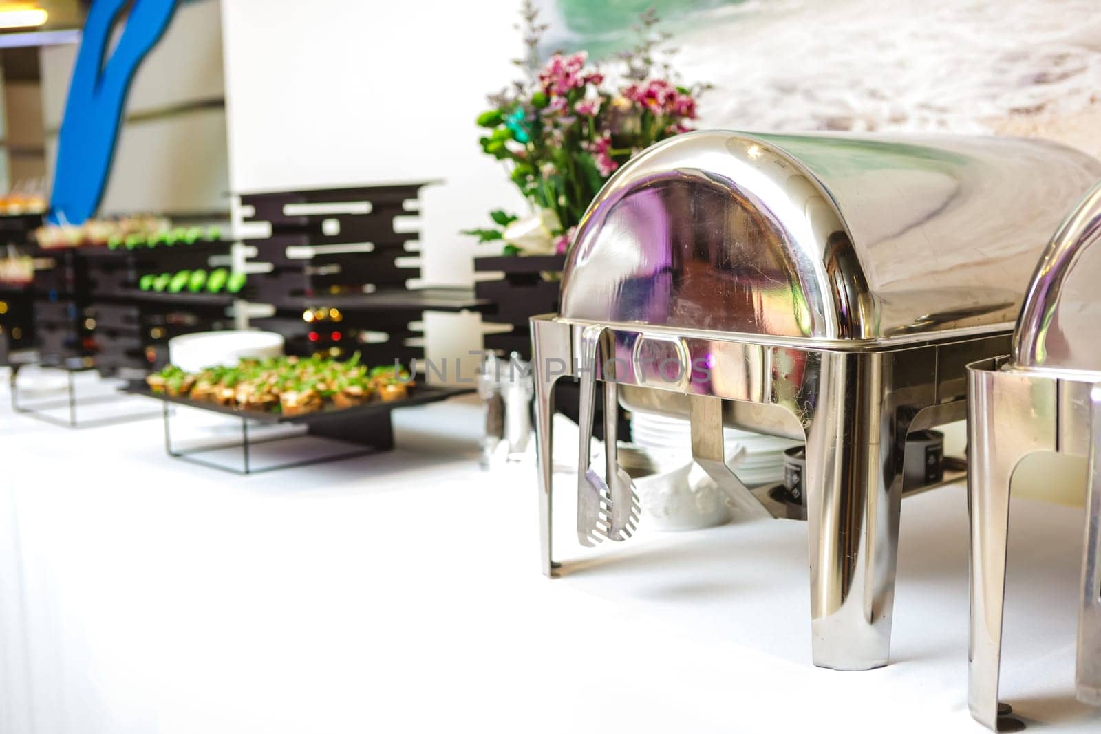 A contemporary hotel dining area featuring a sleek buffet setup and stylish seating arrangement. The space is adorned with modern light fixtures, polished marble floors, and elegant wall decorations.