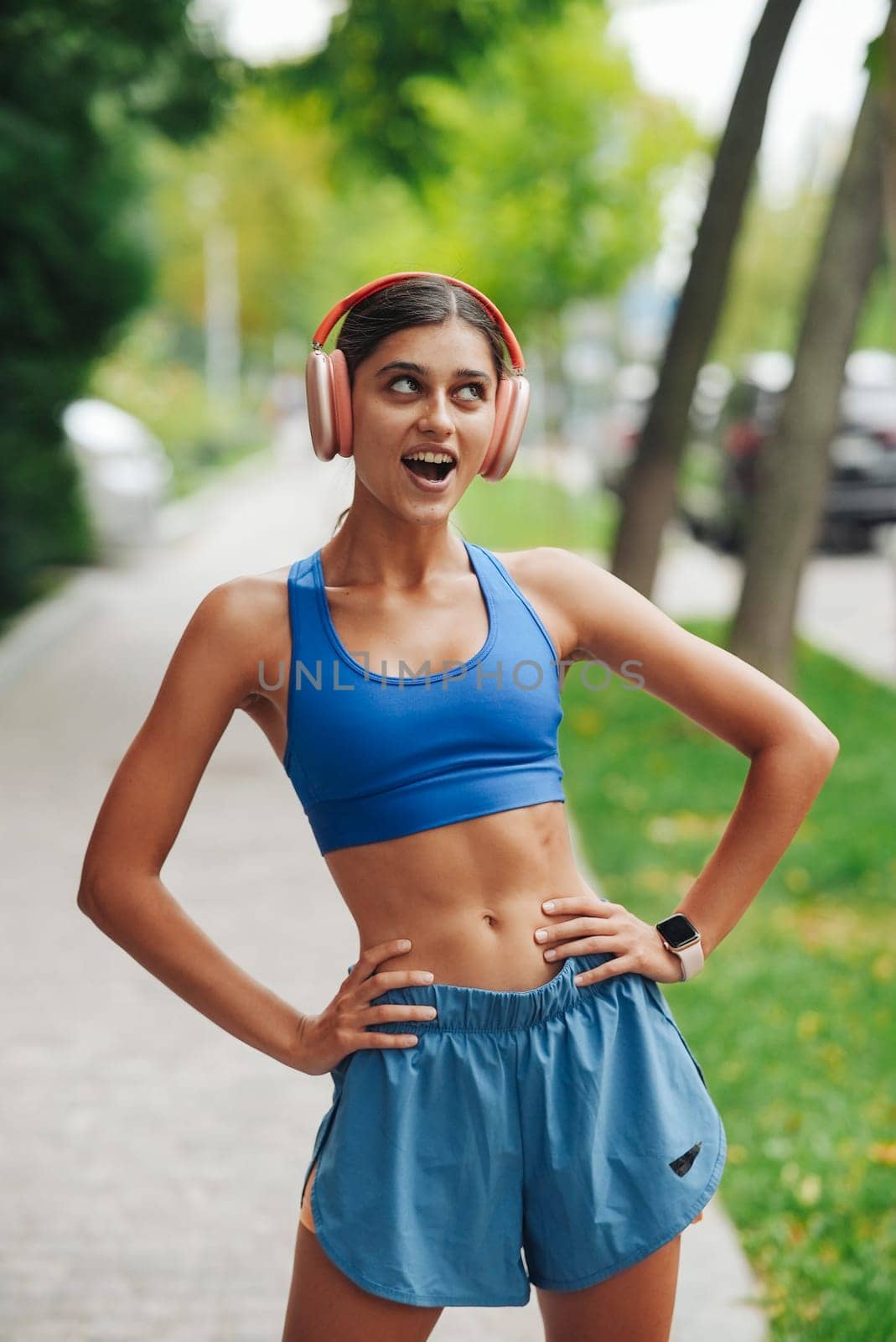 A vibrant and energetic woman dressed in stylish activewear is jogging outdoors while enjoying her favorite music