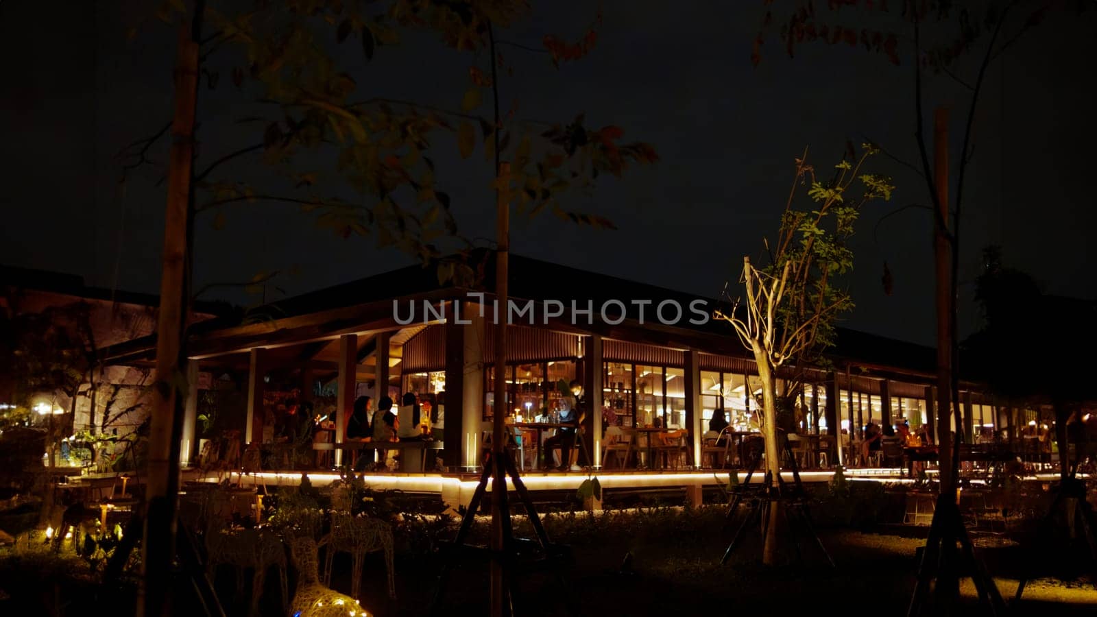 Cozy restaurant exterior at night with warm lighting and silhouettes of people dining inside.