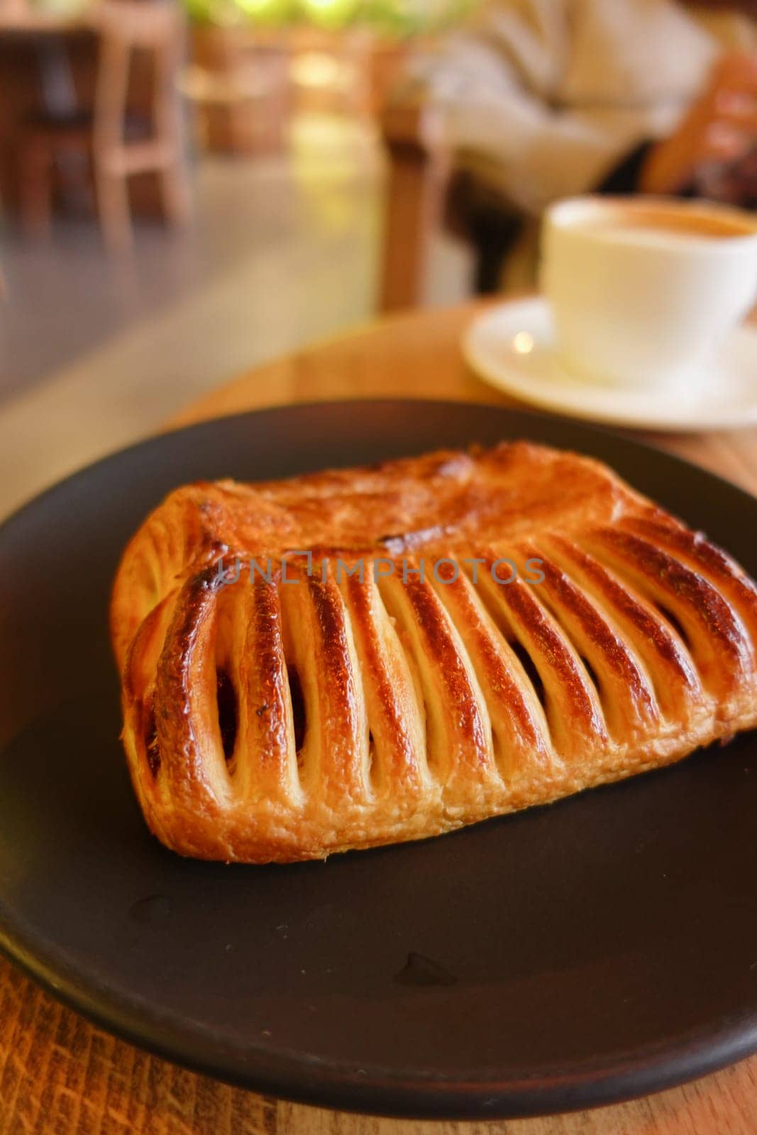 A freshly baked and flaky pastry presented on a dark plate next to a steaming cup of coffee