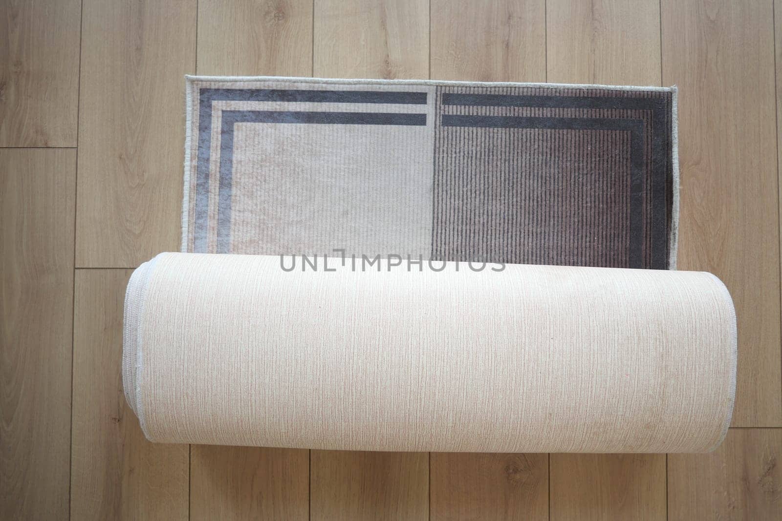 A beautifully designed stylish area rug is currently partially rolled up on a wooden floor