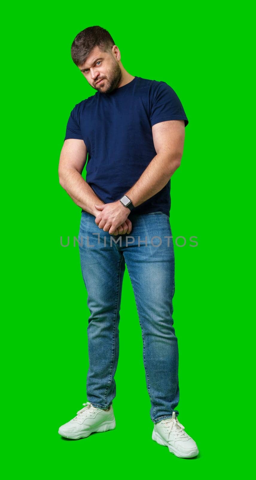 Man standing with a thoughtful expression in a casual outfit against a green background in studio