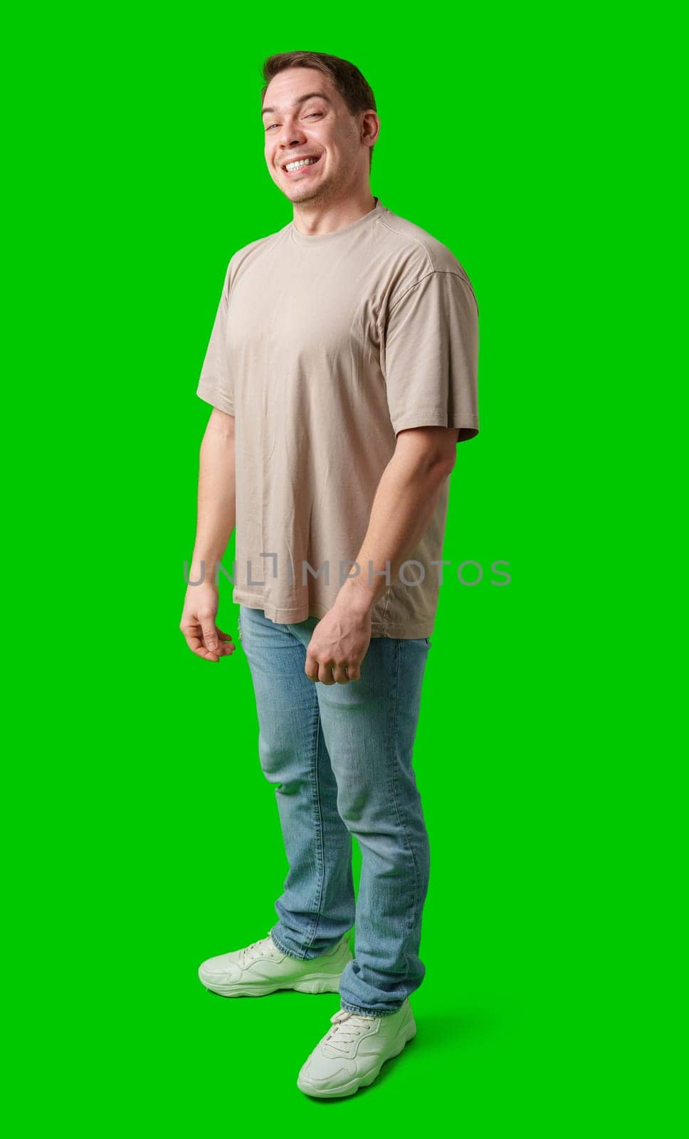 Young man stands confidently in a plain beige t-shirt and jeans against a bright green background in studio