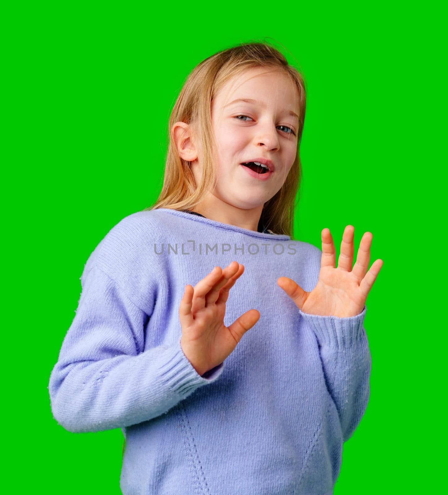 A young girl expresses surprise while smiling, with bright green background and cozy sweater