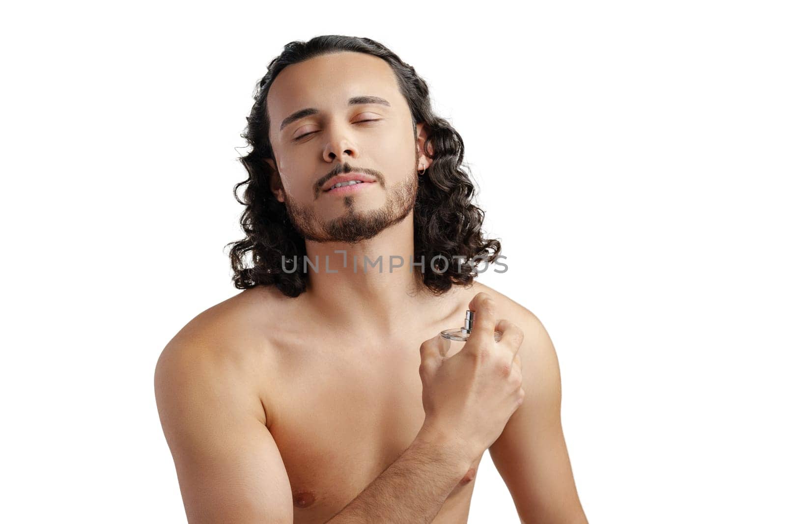 A young man with curly hair applying fragrance after a shower while smiling at the camera close up
