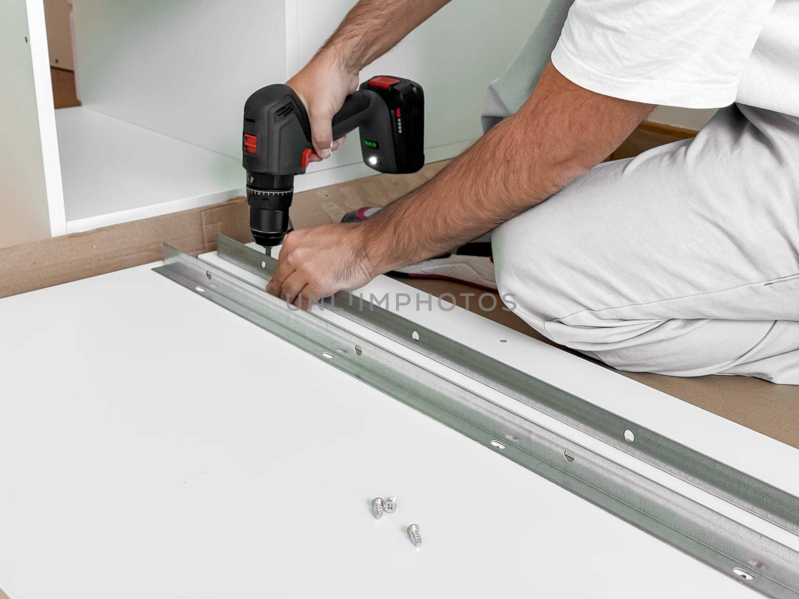 Caucasian male adult assembling furniture with electric drill in workshop.