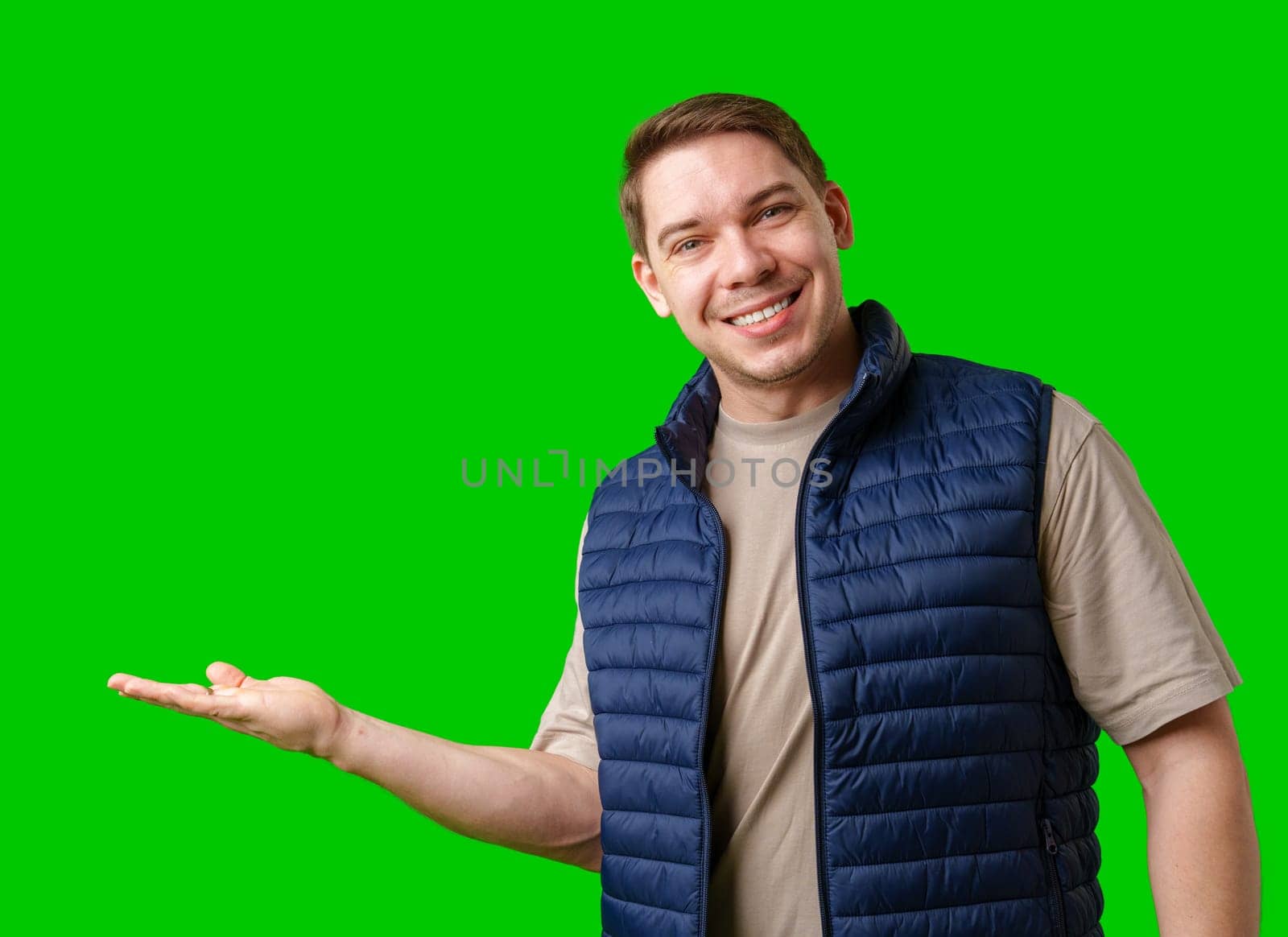 Man in a navy vest gestures while standing against a bright green background in studio