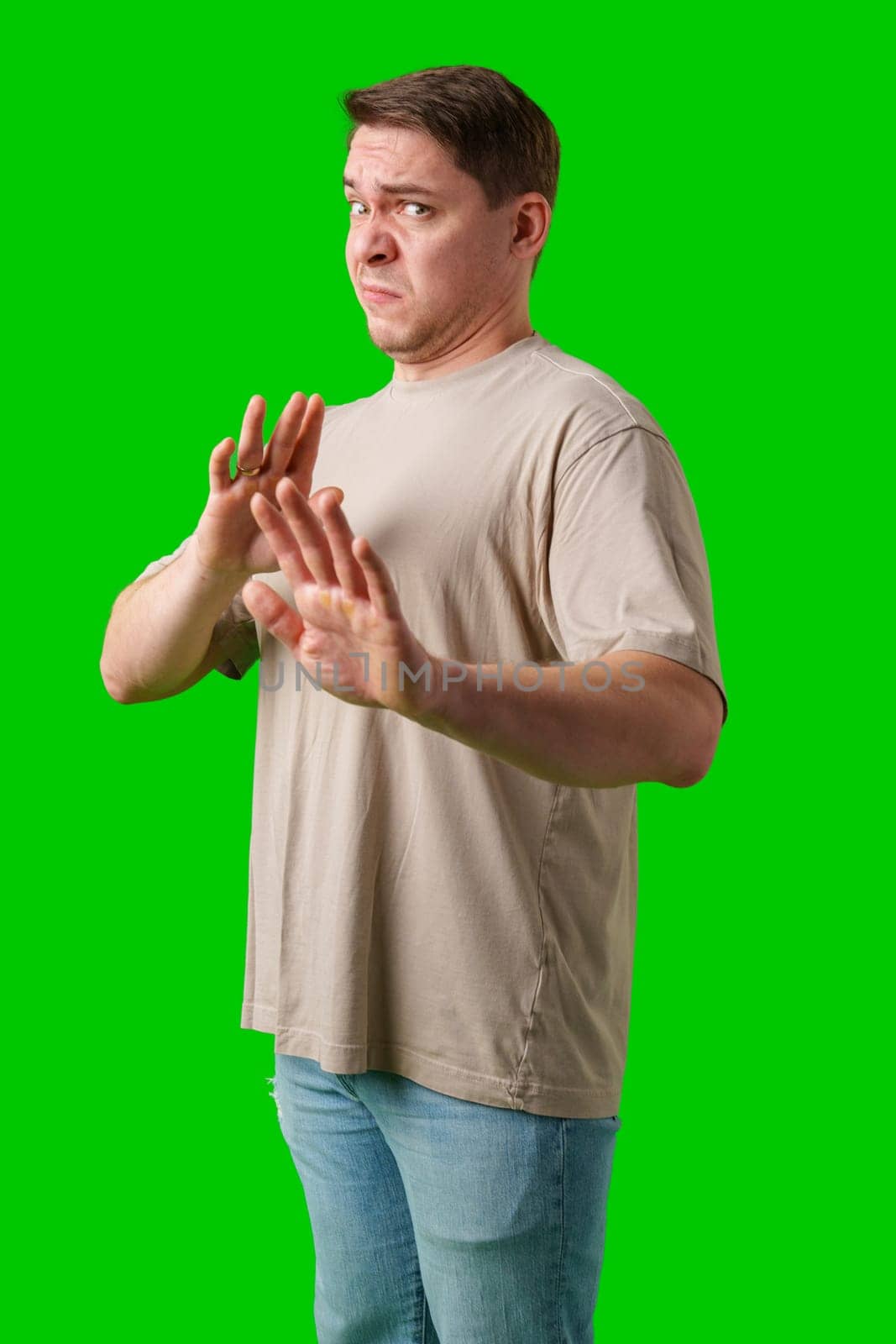 A man with a neutral expression gestures defensively against a bright green background in studio