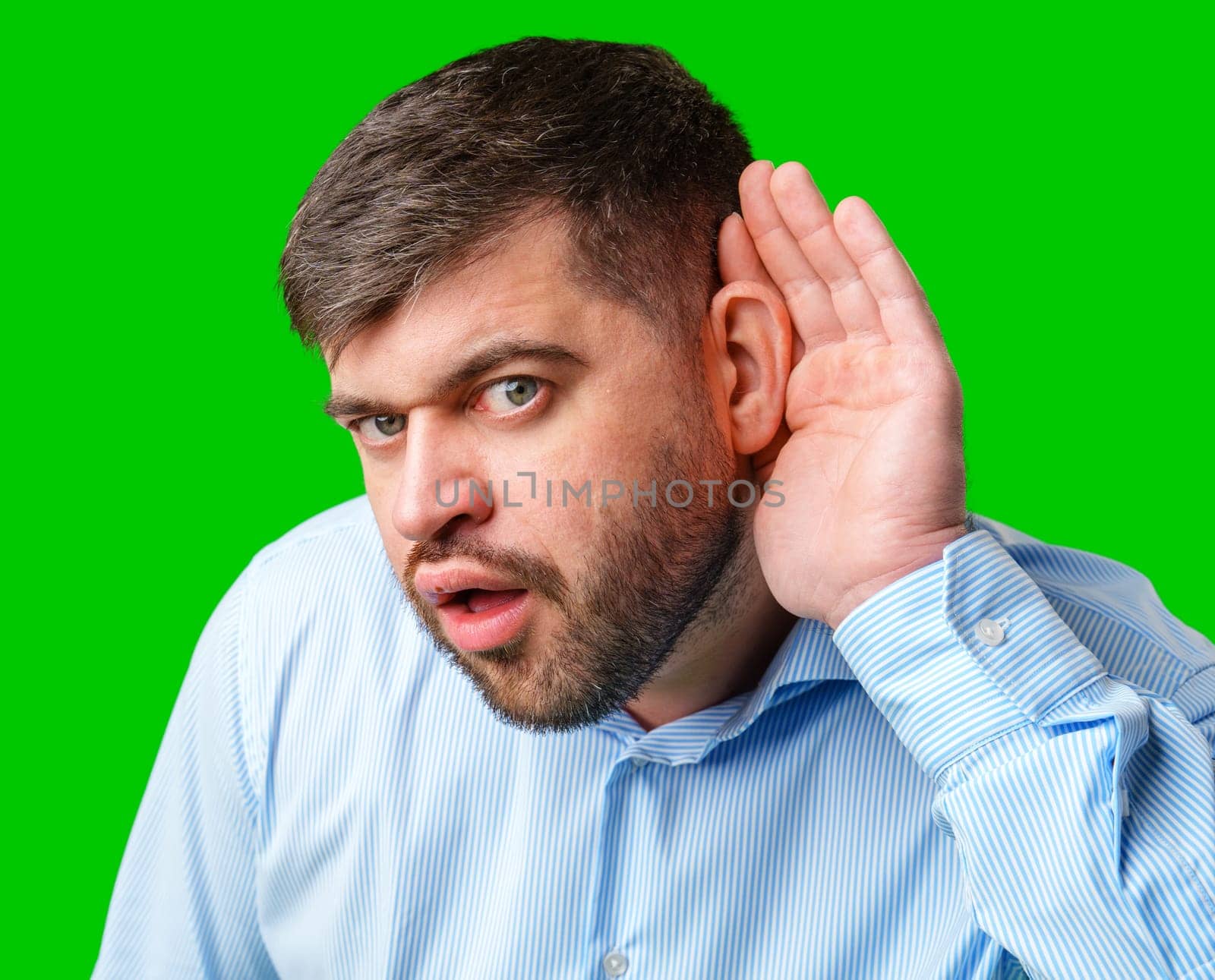 A man listening intently with a surprised expression in a bright green background in studio