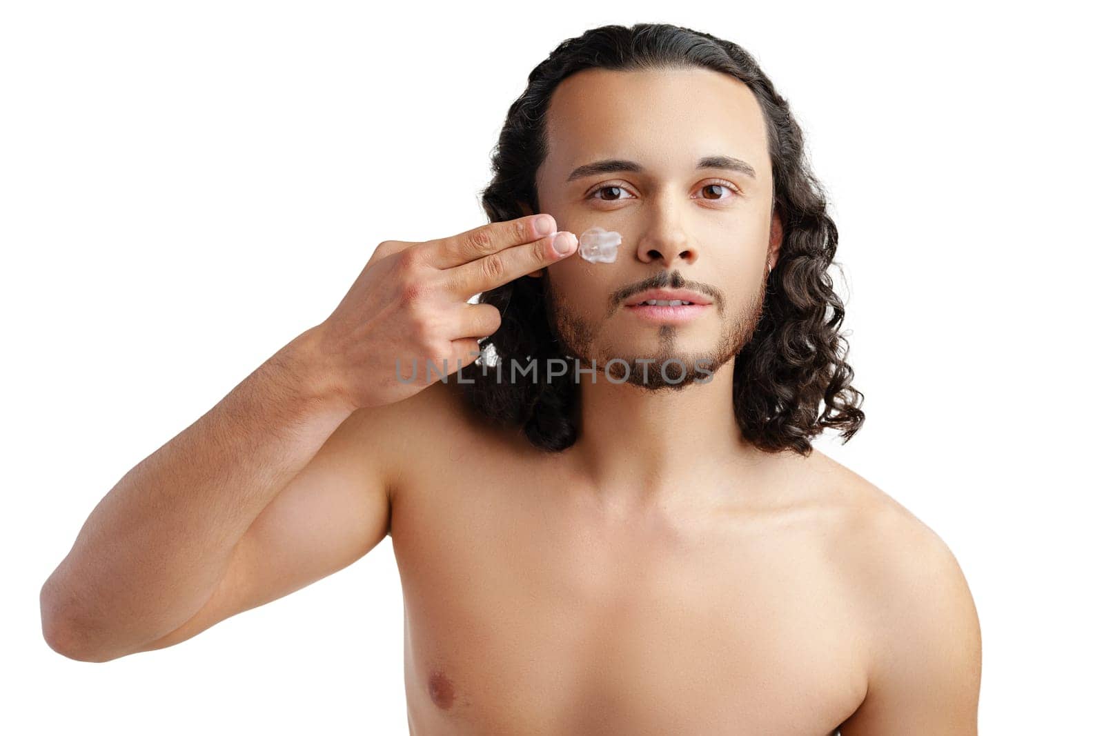 A young man demonstrates skincare routine with moisturizer on his face close up
