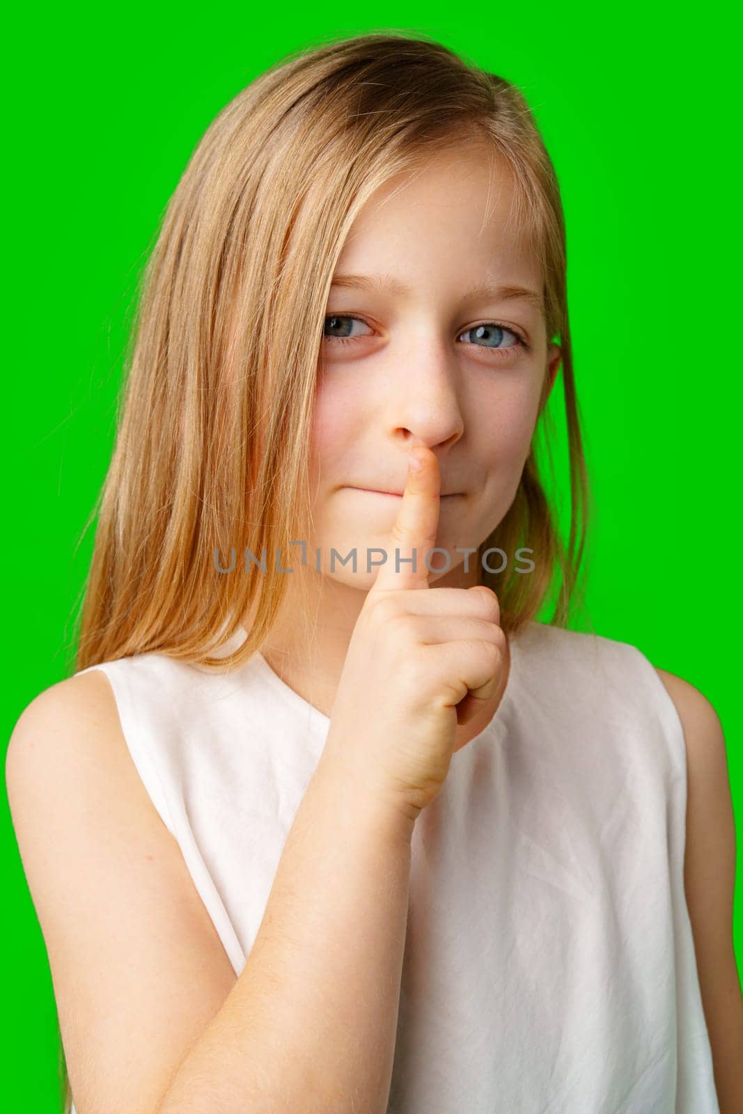 Young girl playfully signaling for silence with a finger to her lips against a vibrant green background in studio