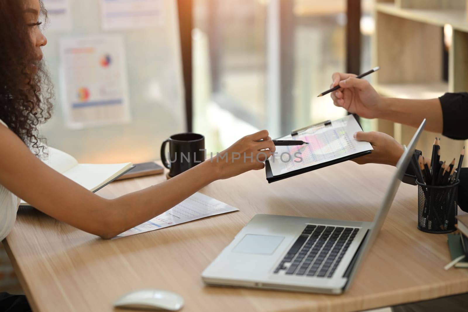 Cropped shot two professional businesspeople discussing data on clipboard in modern workspace.