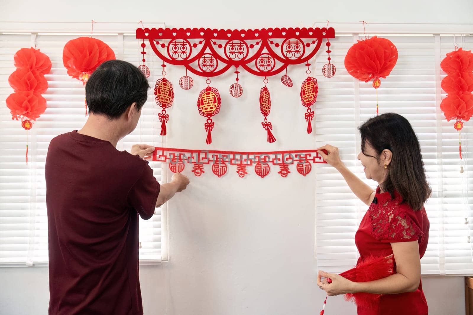 An elderly couple joyfully decorates their home for Chinese New Year showcasing traditions and family togetherness.