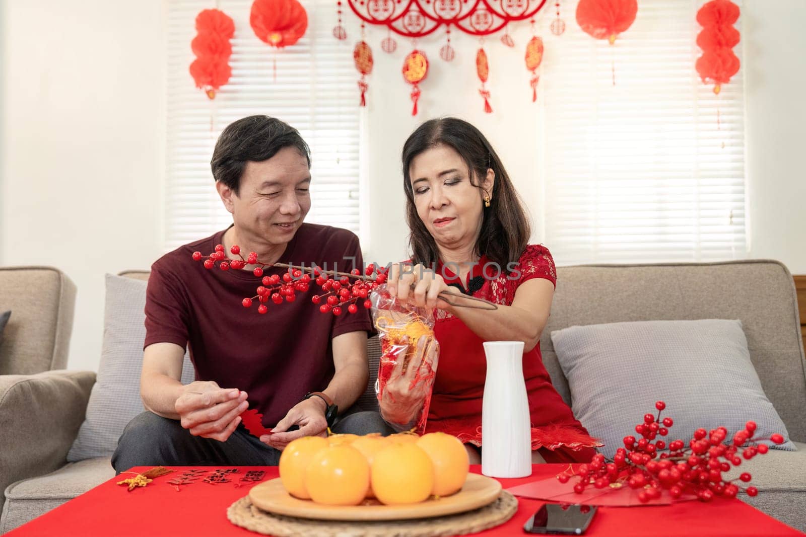 An elderly couple joyfully prepares for Chinese New Year surrounded by festive decorations and traditional symbols of good fortune.