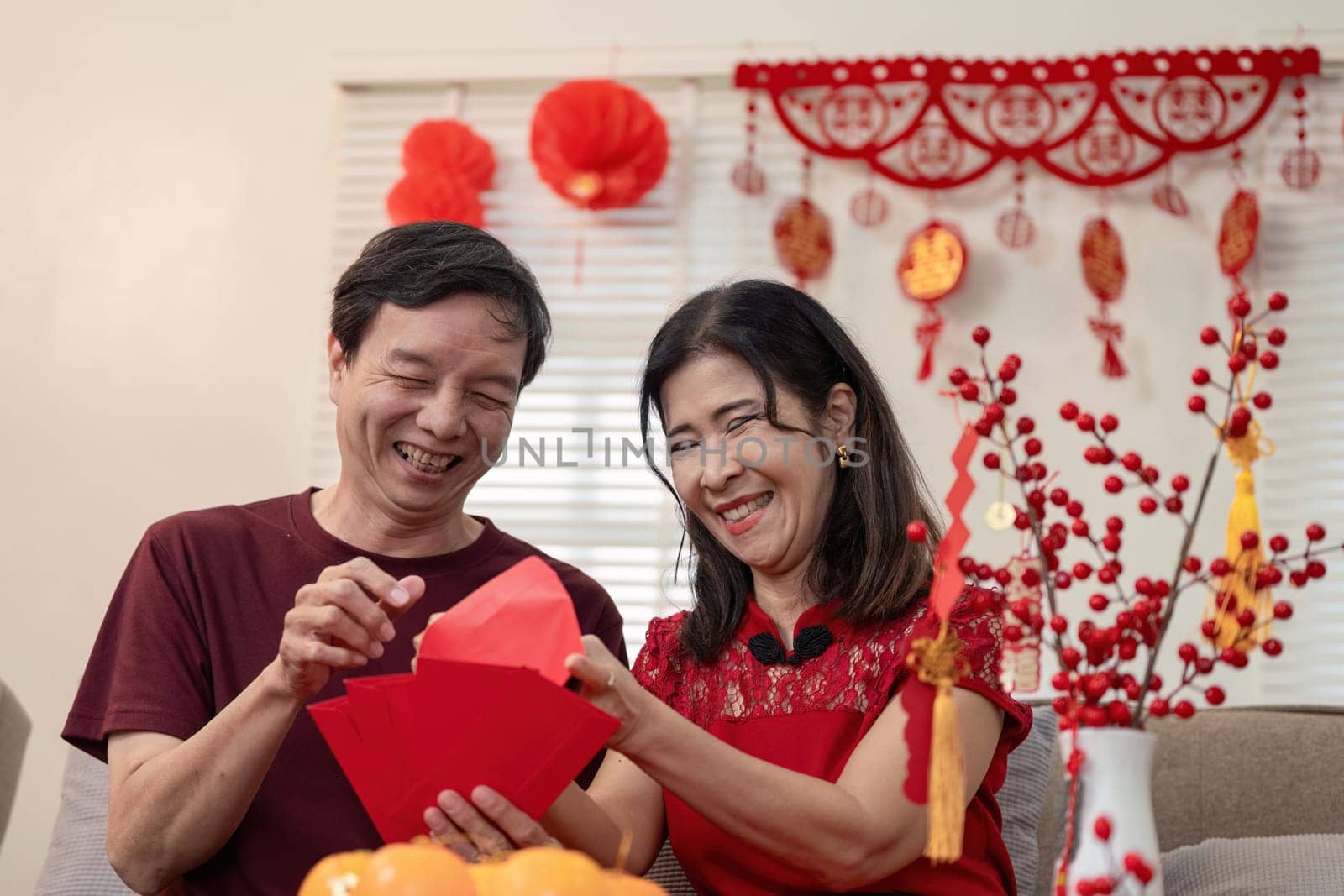 An elderly couple joyfully celebrates Chinese New Year at home surrounded by colorful decorations and shared happiness.