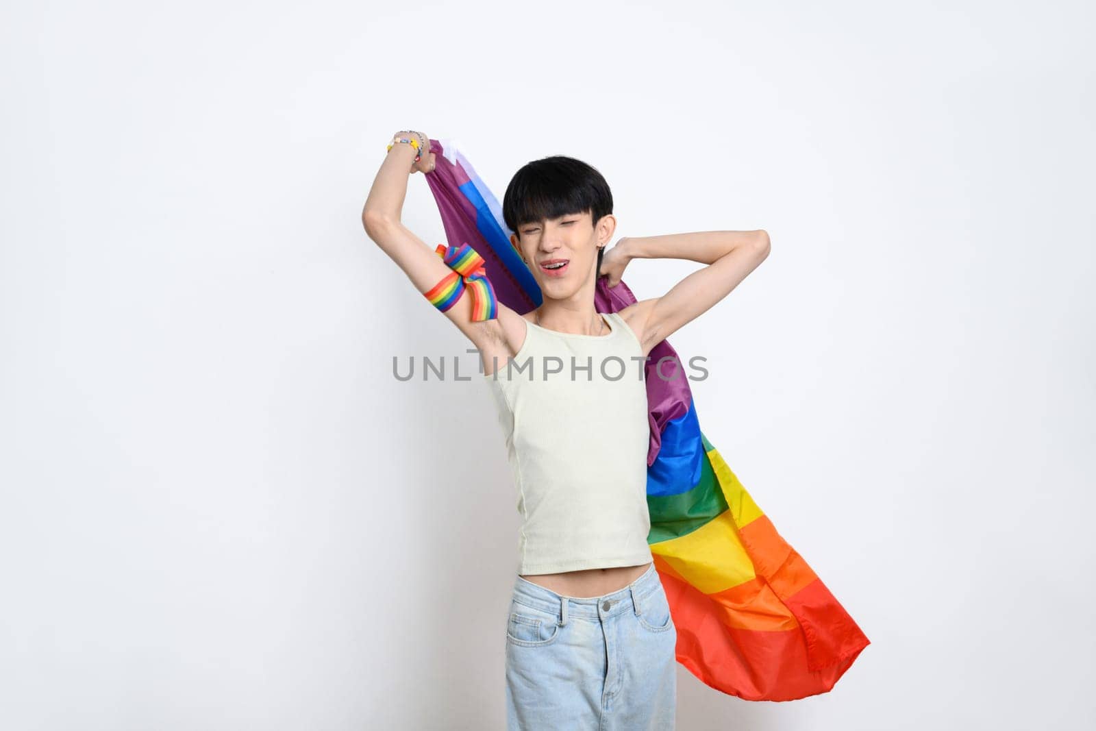 Cheerful young gay man holding a rainbow pride flag on white background. LGBTQ pride and equality concept.
