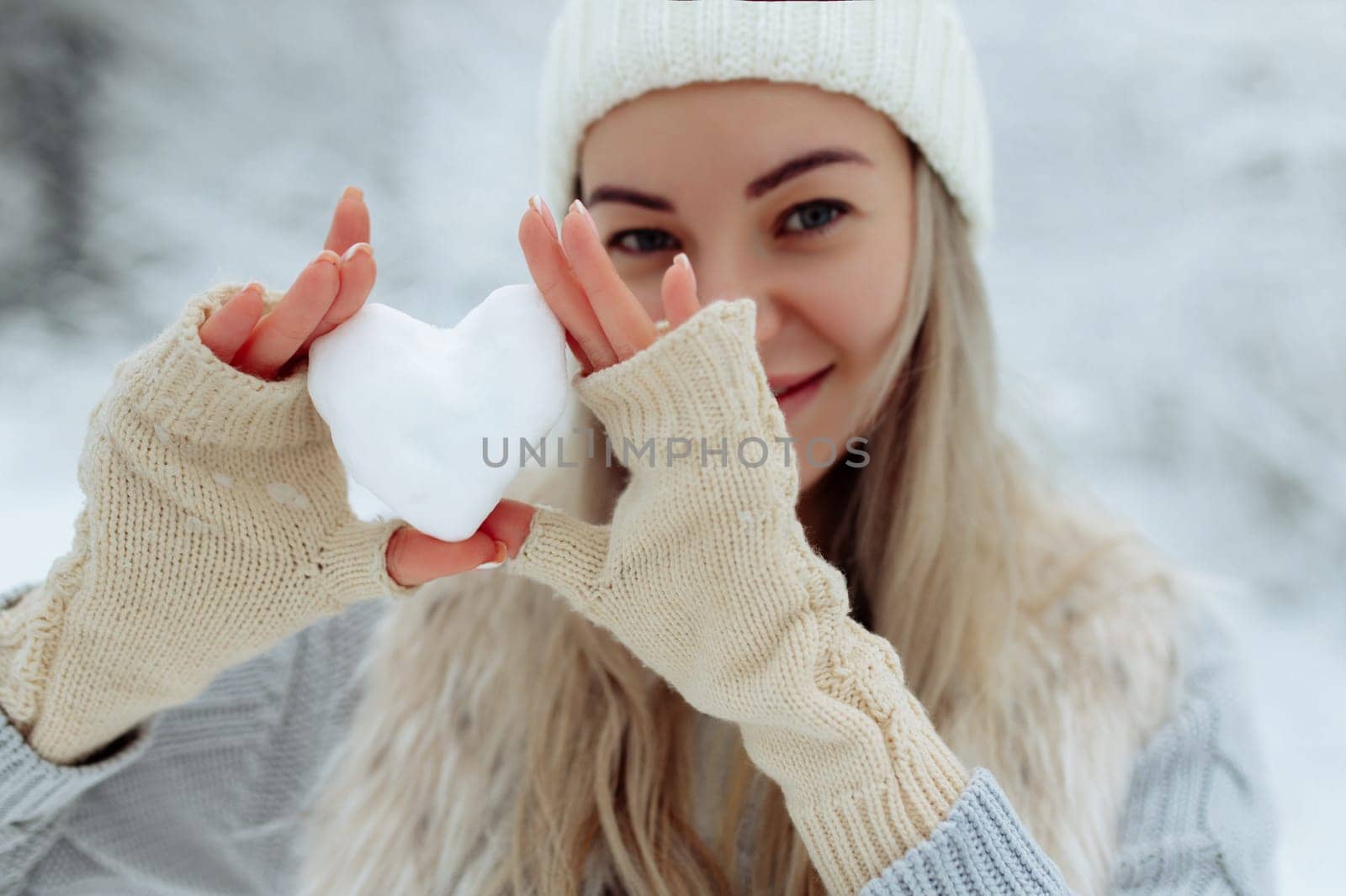 Close-up girl holds a snowy heart in front of her in gloves.