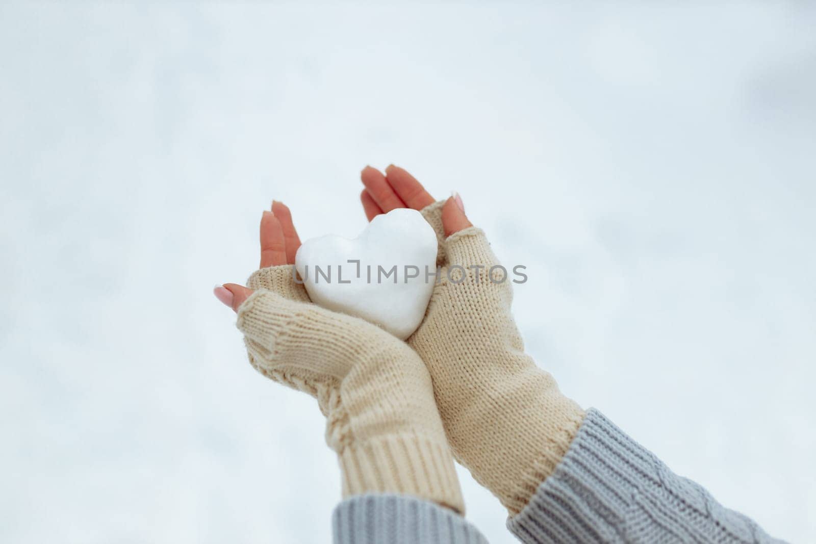 Close-up Snow heart in hands in knitted gloves on the background of snow cover. Valentine's Day.