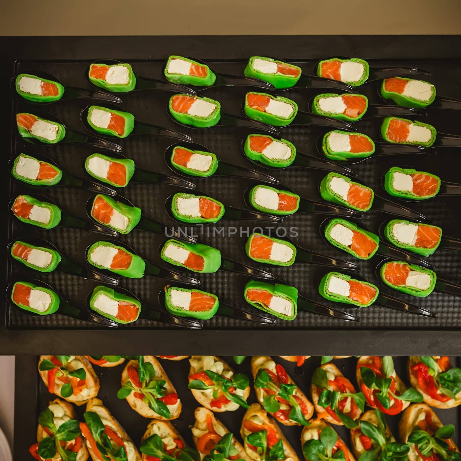 Platter of gourmet appetizers featuring pieces of salmon and cream cheese wrapped in a green wrap, served on black spoons. The presentation is elegant and suitable for catering events or parties