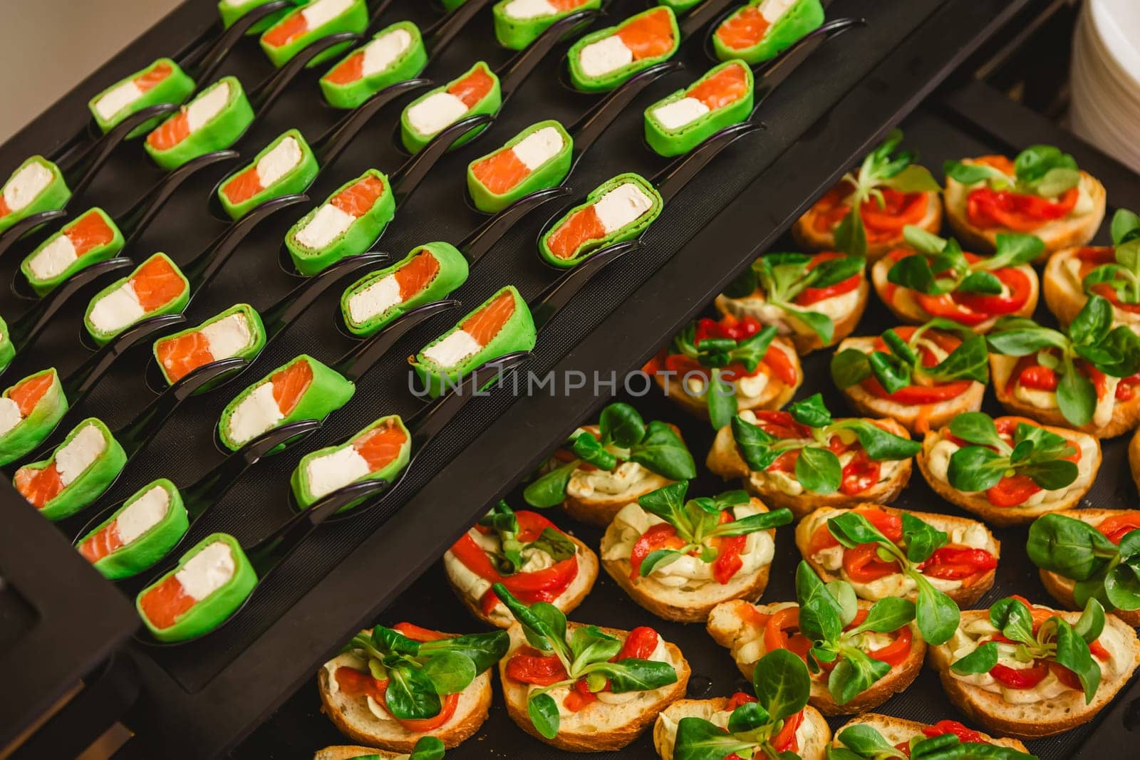 Platter of gourmet appetizers featuring pieces of salmon and cream cheese wrapped in a green wrap, served on black spoons. The presentation is elegant and suitable for catering events or parties