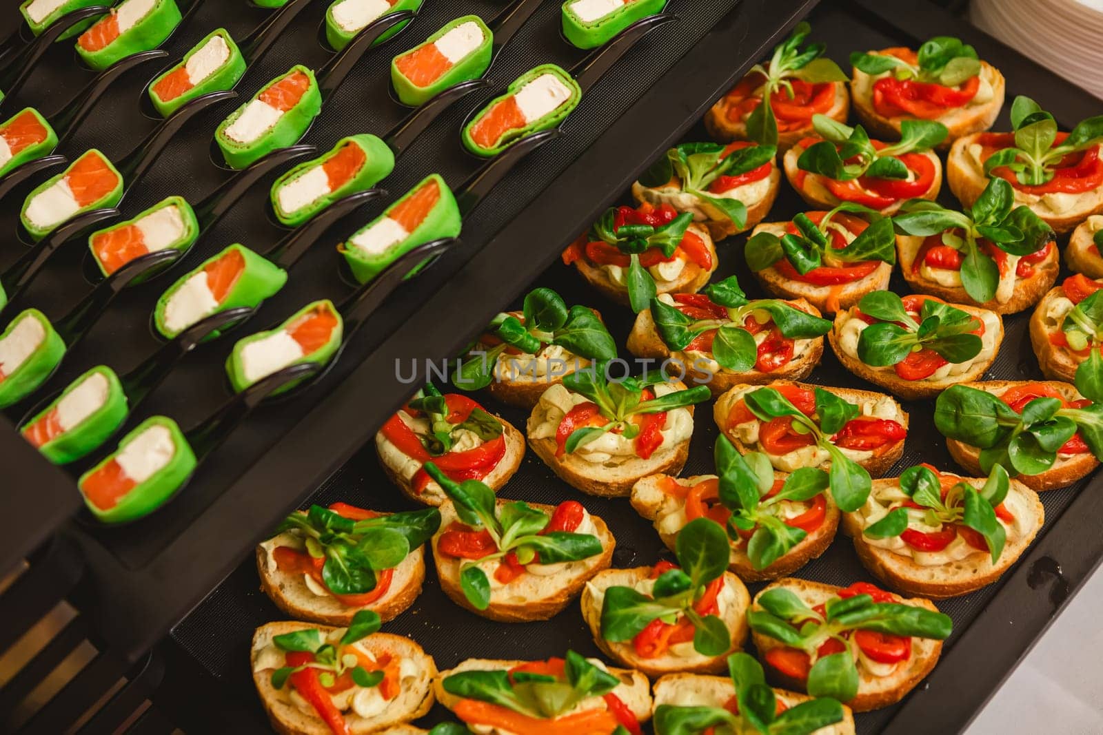 Platter of gourmet appetizers featuring pieces of salmon and cream cheese wrapped in a green wrap, served on black spoons. The presentation is elegant and suitable for catering events or parties