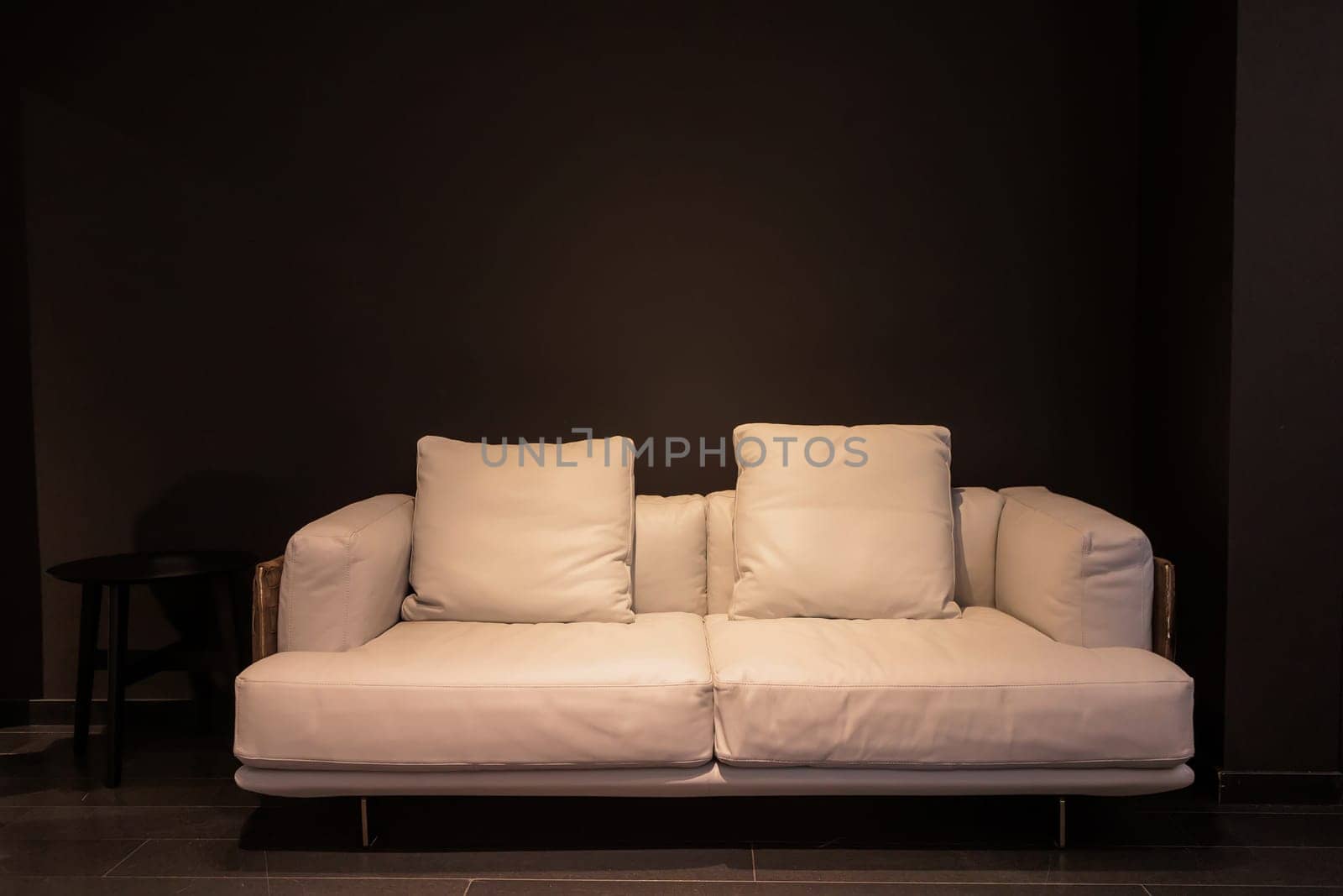 Designed white sofa with two cushions is set against a stark black background, complemented by a small black side table.