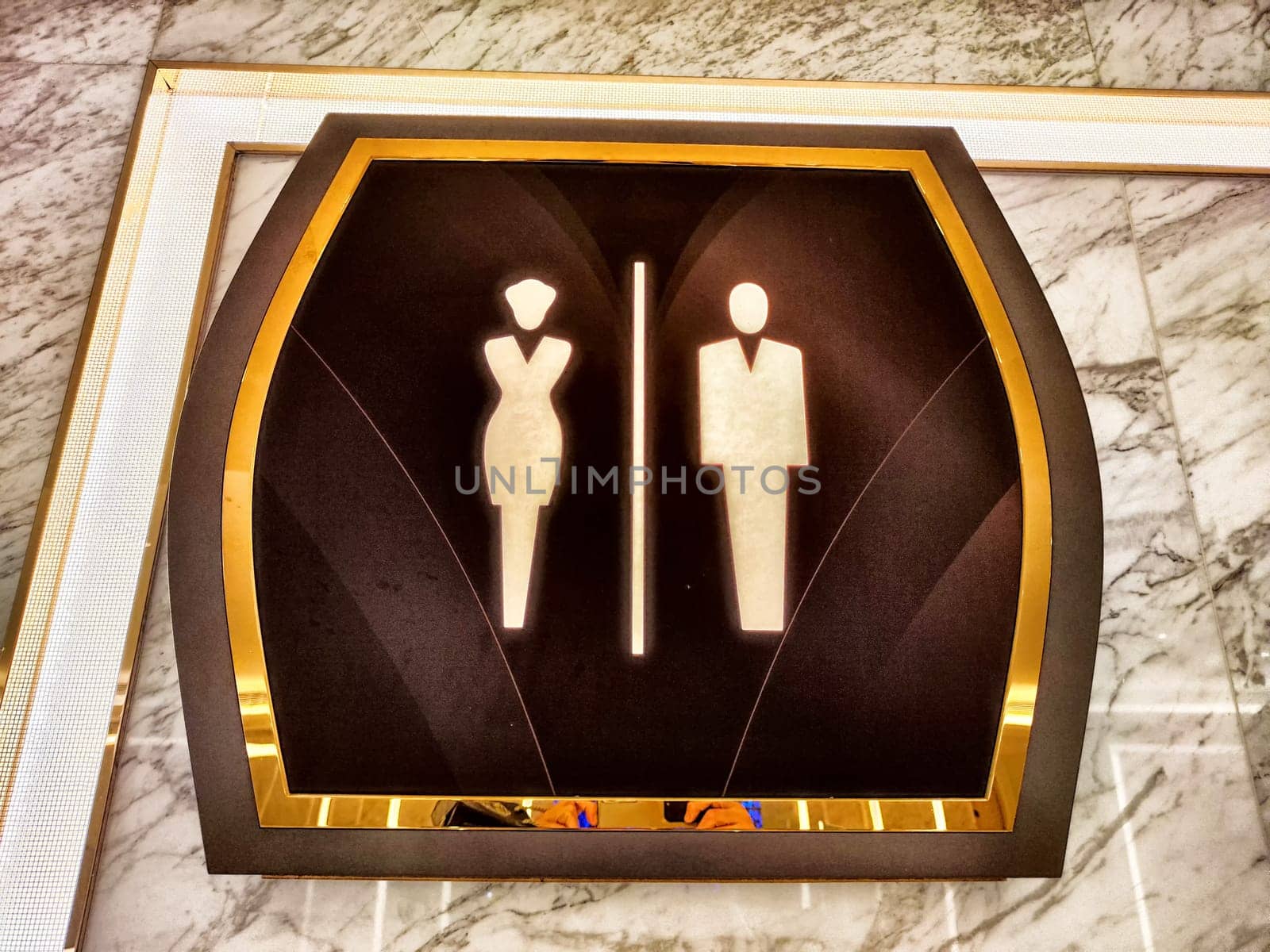 A stylish restroom sign features clear male and female icons, set against a well-lit marble wall, indicating facilities.