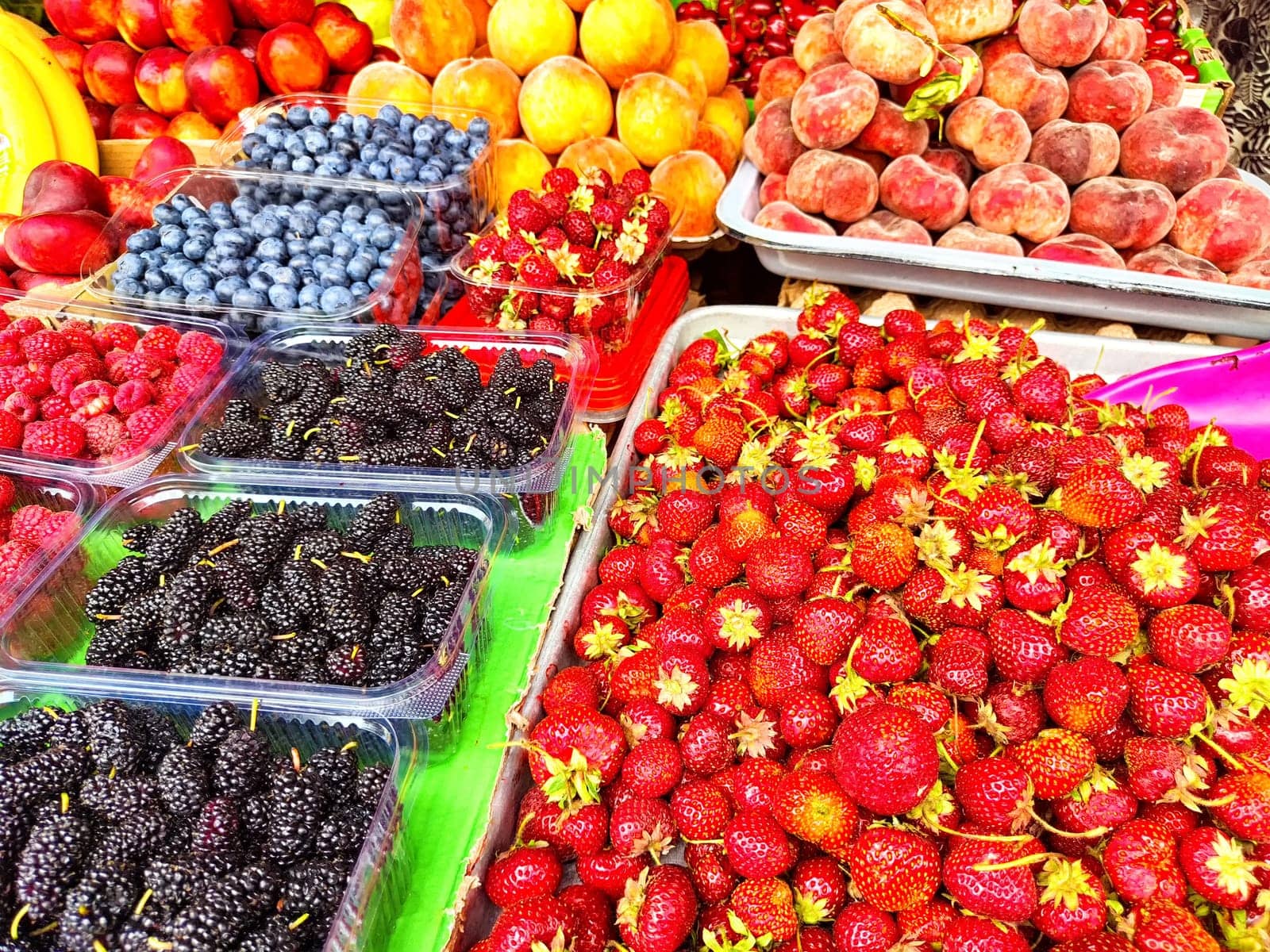 Brightly colored berries and fruits fill the market stand, showcasing strawberries, blueberries, and raspberries in midday light.