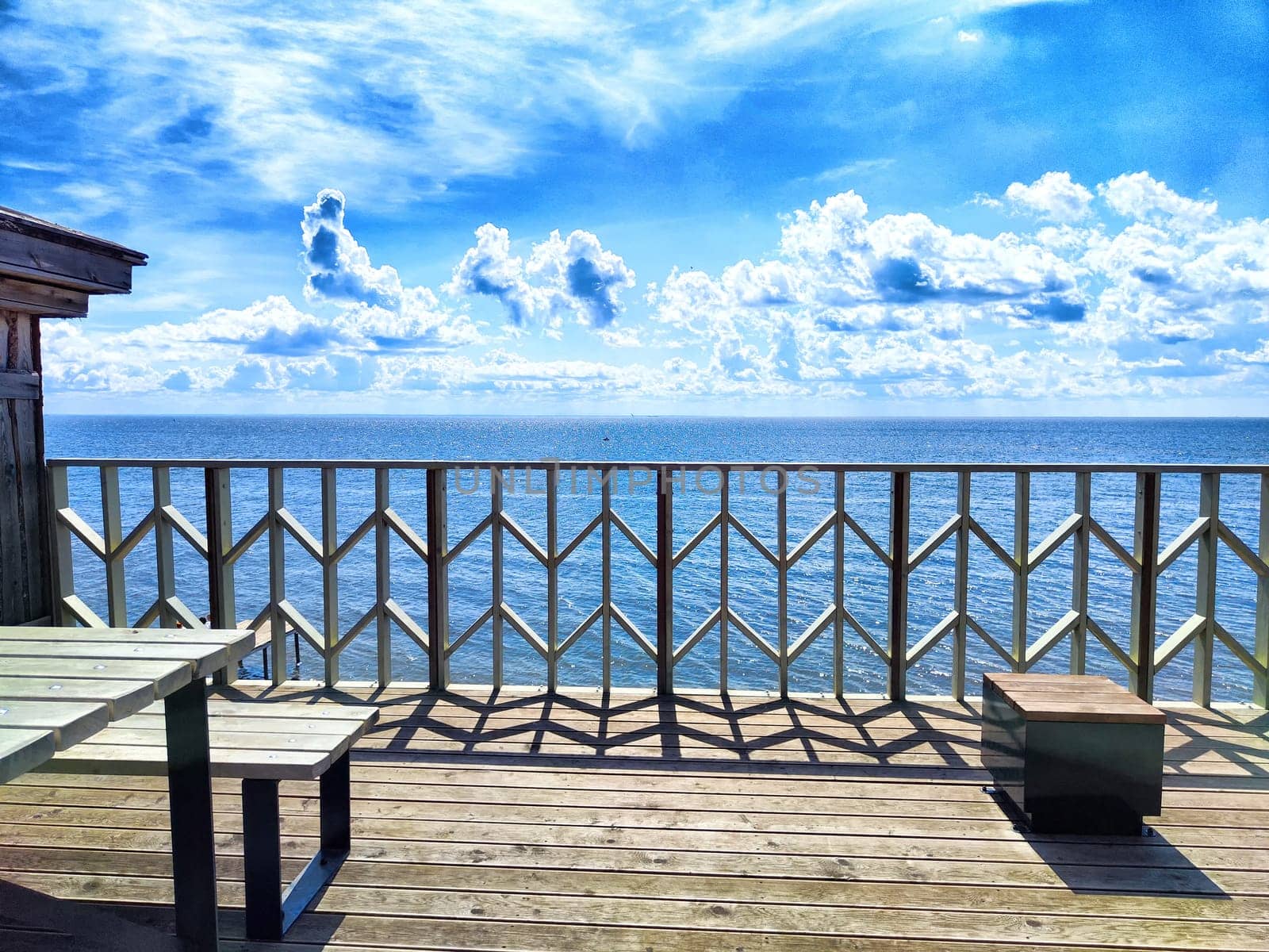 A beautiful wooden deck overlooks the sparkling ocean, with clear blue skies and soft clouds enhancing the tranquil atmosphere.