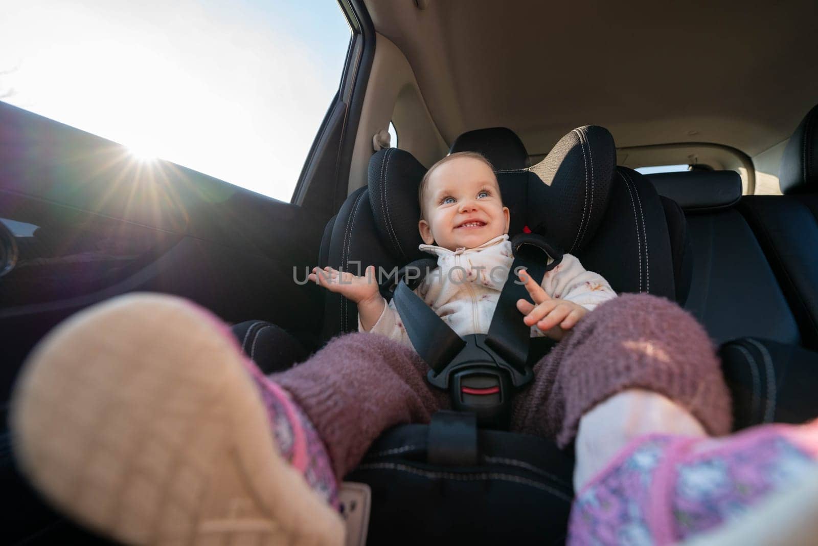 A cheerful baby seated securely in a car seat, smiling with sunlight streaming in during a family road trip. Concept of safe travel, happiness, and comfort for young passengers