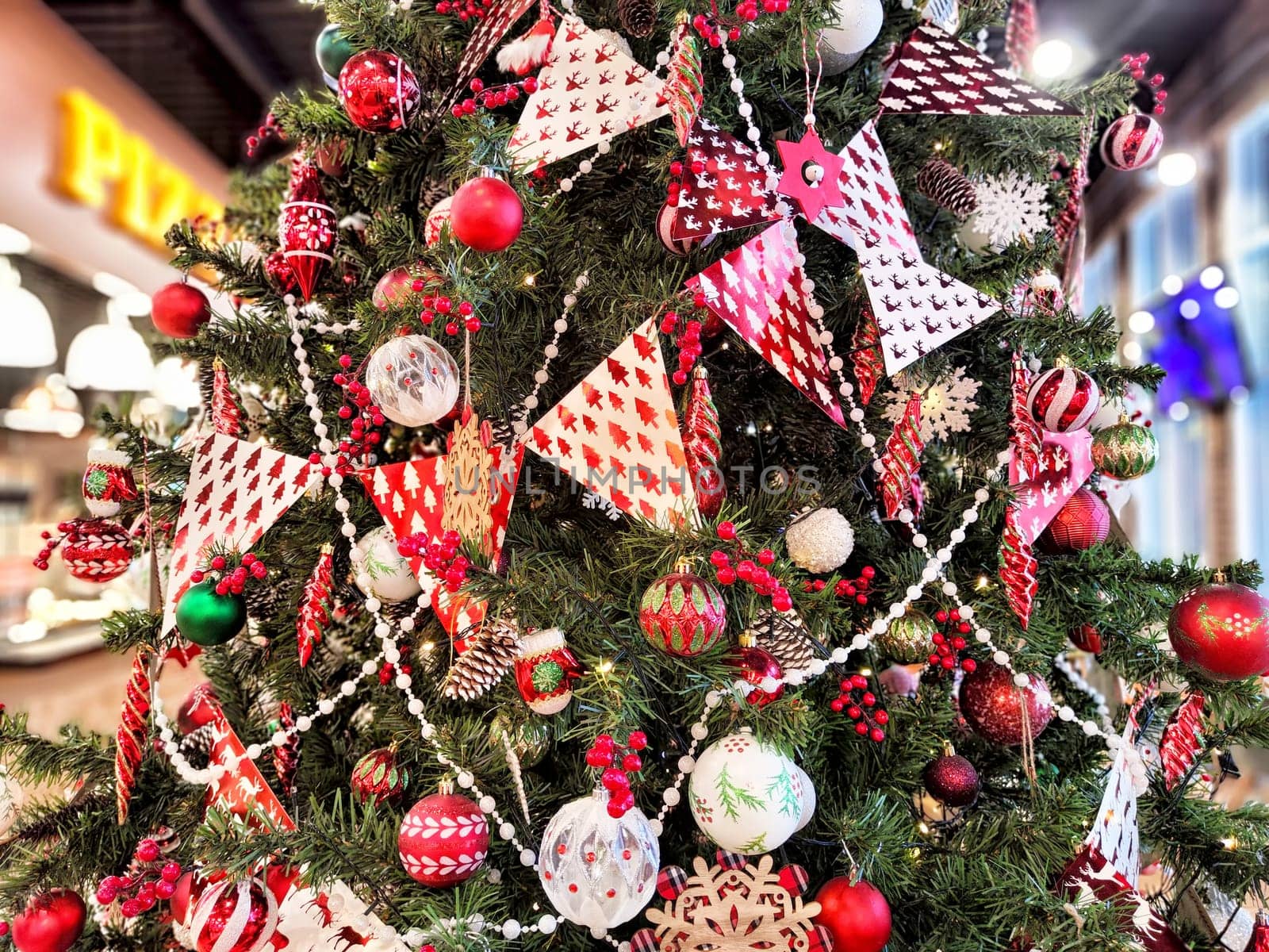 A beautifully adorned Christmas tree stands in a lively indoor area, featuring red and white decorations, ornaments, and garlands.