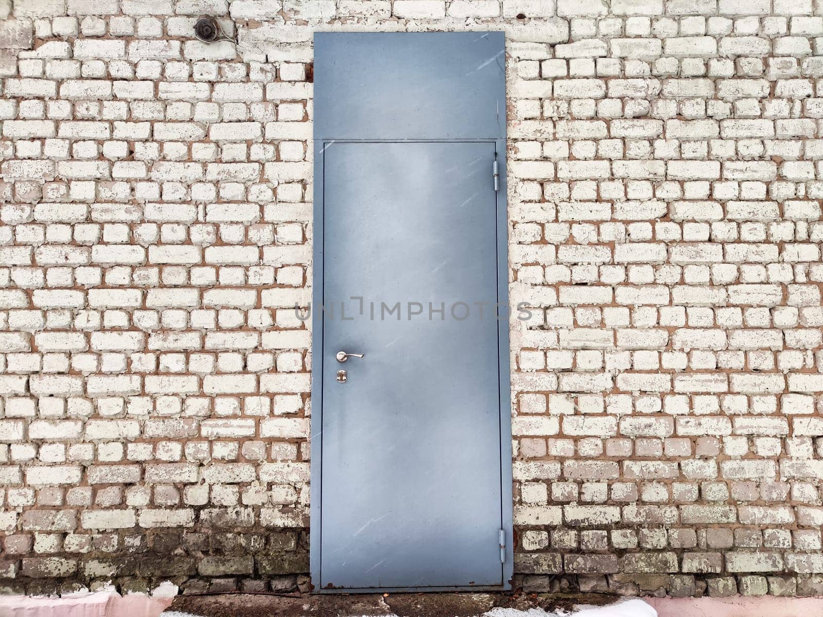 Gray door integrated into a textured brick wall, highlighting natural light and outdoor setting on a clear day.