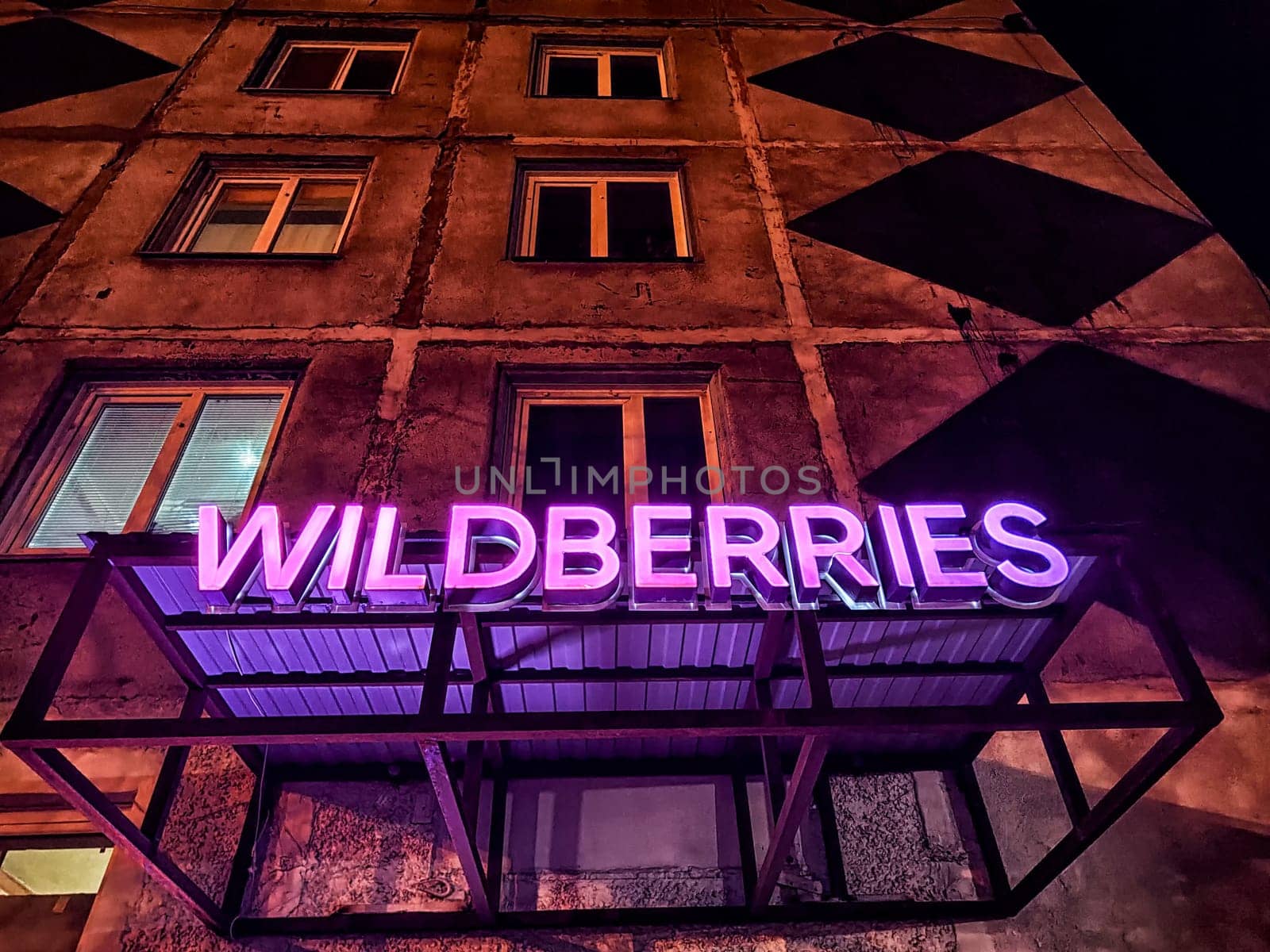 Novosibirsk, Russia - November 06, 2024: A vibrant neon logo glows prominently, showcasing a marketplace against the backdrop of a textured urban building.