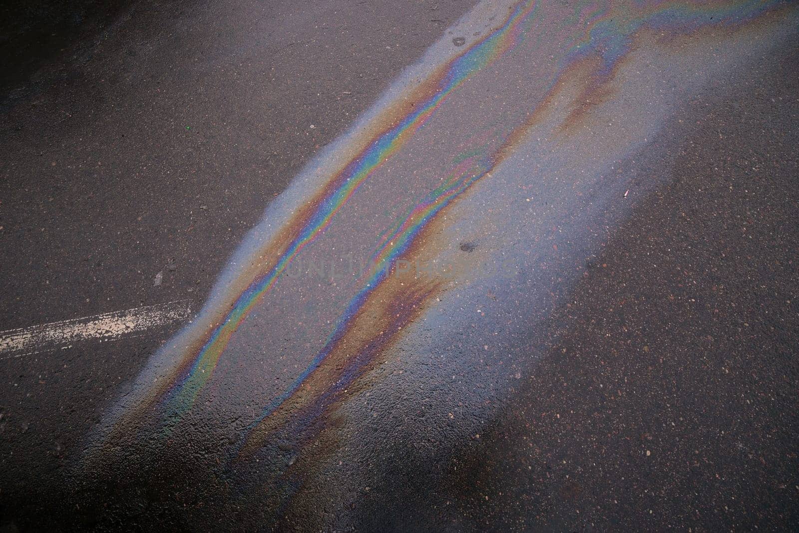 Colorful gasoline spill polluting wet asphalt road creating a rainbow effect.