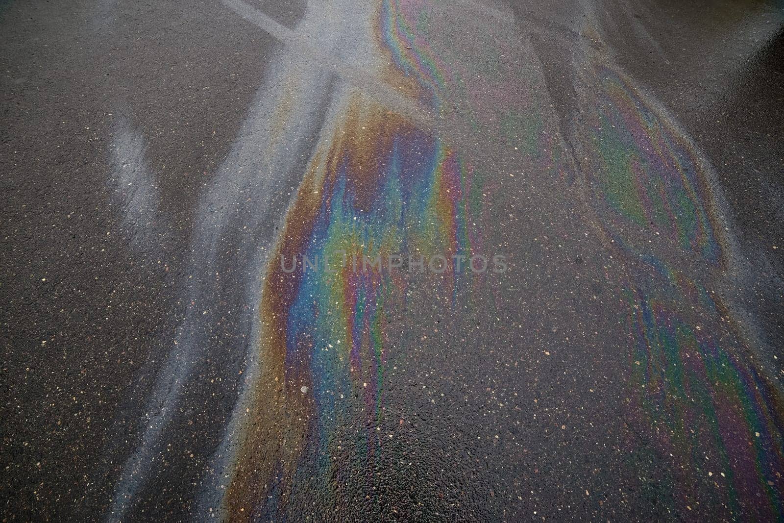 Gasoline rainbow on wet asphalt creates pollution.