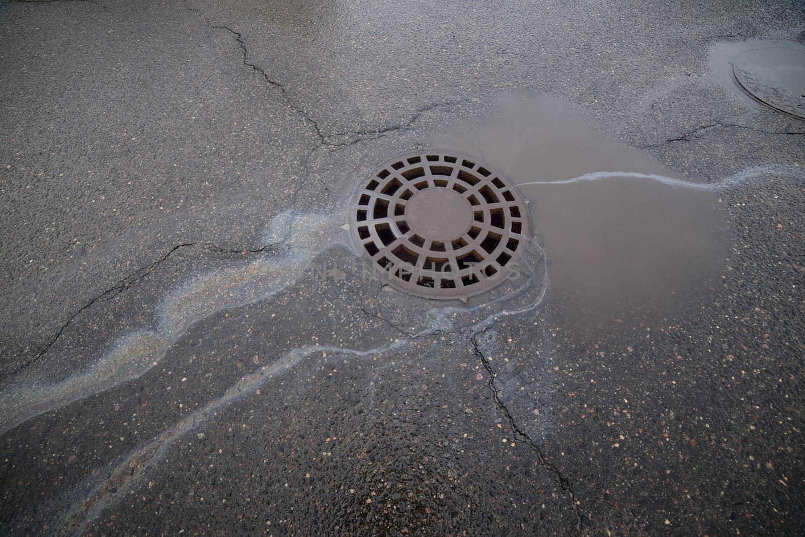 Gasoline or oil flowing into a storm drain on a cracked asphalt road.