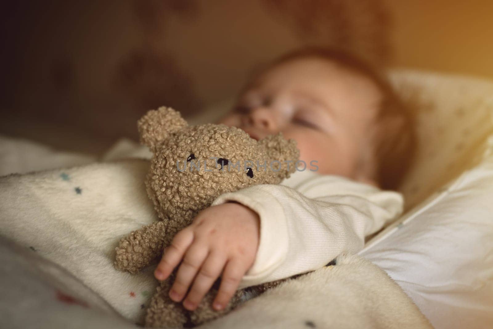 Sleeping newborn baby lying with a soft teddy bear under the blanket in warm, cozy sunlight. Childhood and parenting concept. High quality photo