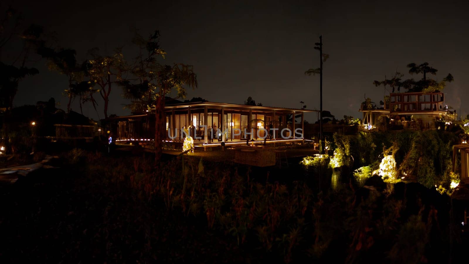 Tropical resort at night with illuminated bungalow and palm trees in the dark night