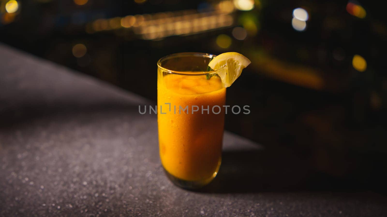 Frosty mango cocktail with lime garnish on a dark bar counter, with blurred background in the dark night
