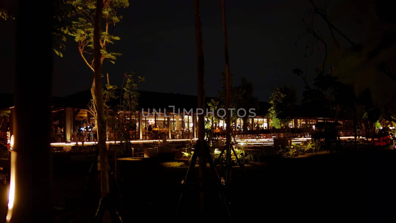 Nighttime view of a tranquil outdoor restaurant with ambient lighting and trees in the dark night