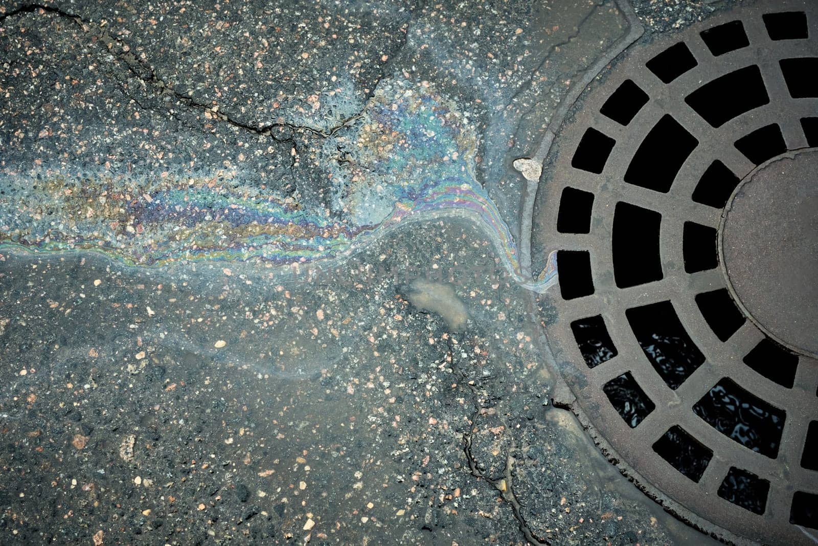 Gasoline or oil spill flowing to storm drain on asphalt.