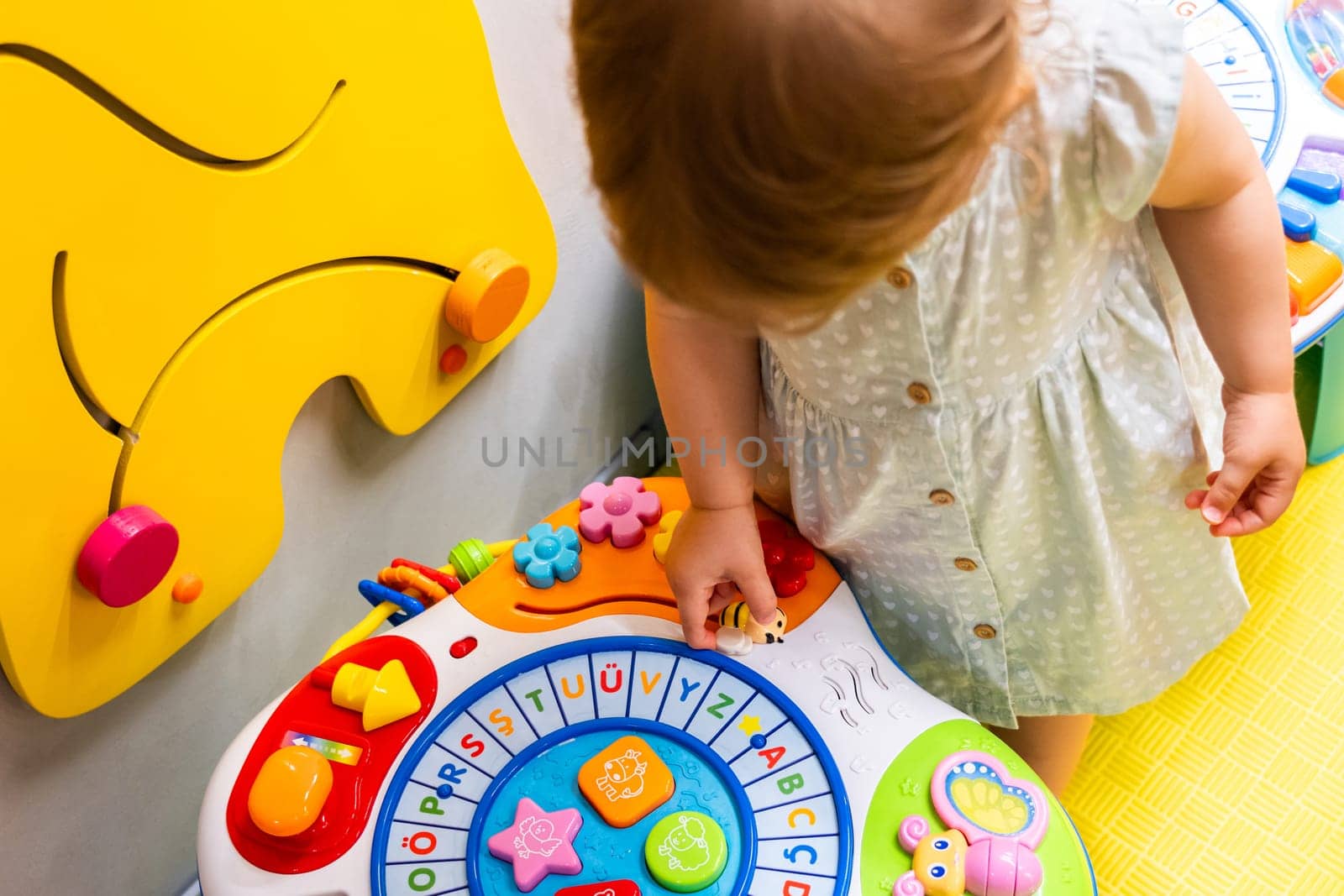 Toddler playing with an interactive toy designed for learning shapes and colors in a colorful playroom. Concept of combining fun and education to promote early development