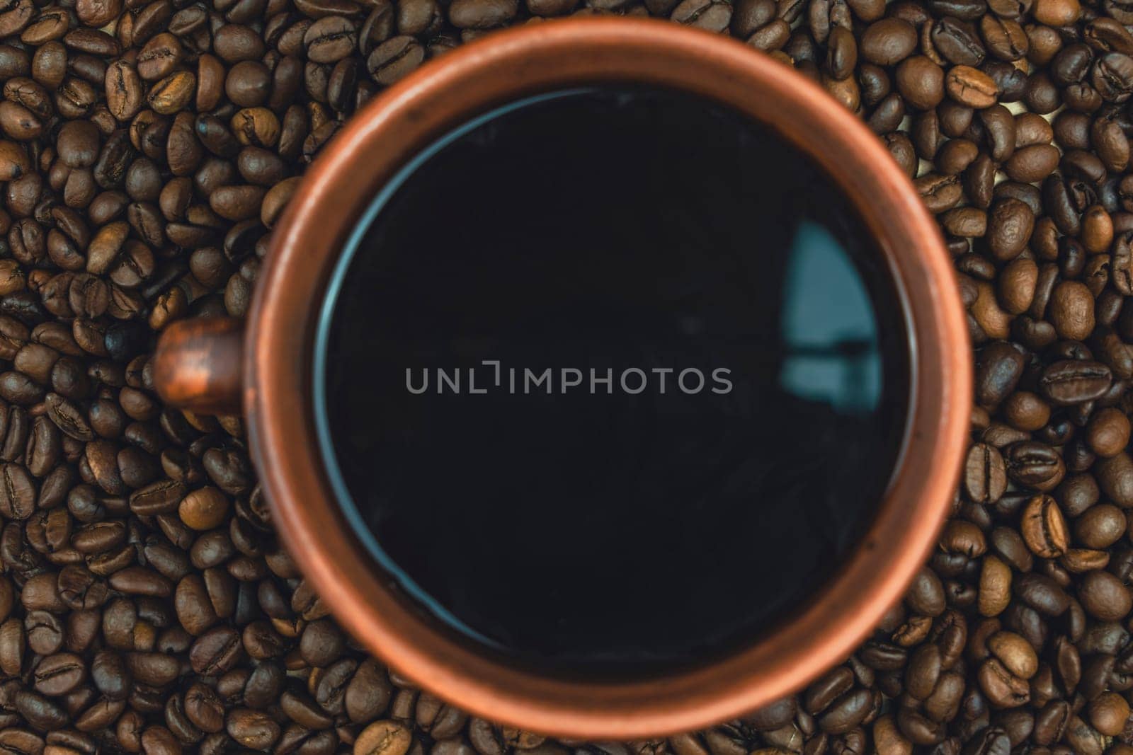 Overhead view of a clay cup filled with black coffee surrounded by roasted coffee beans, creating a rustic and textured composition, no people.