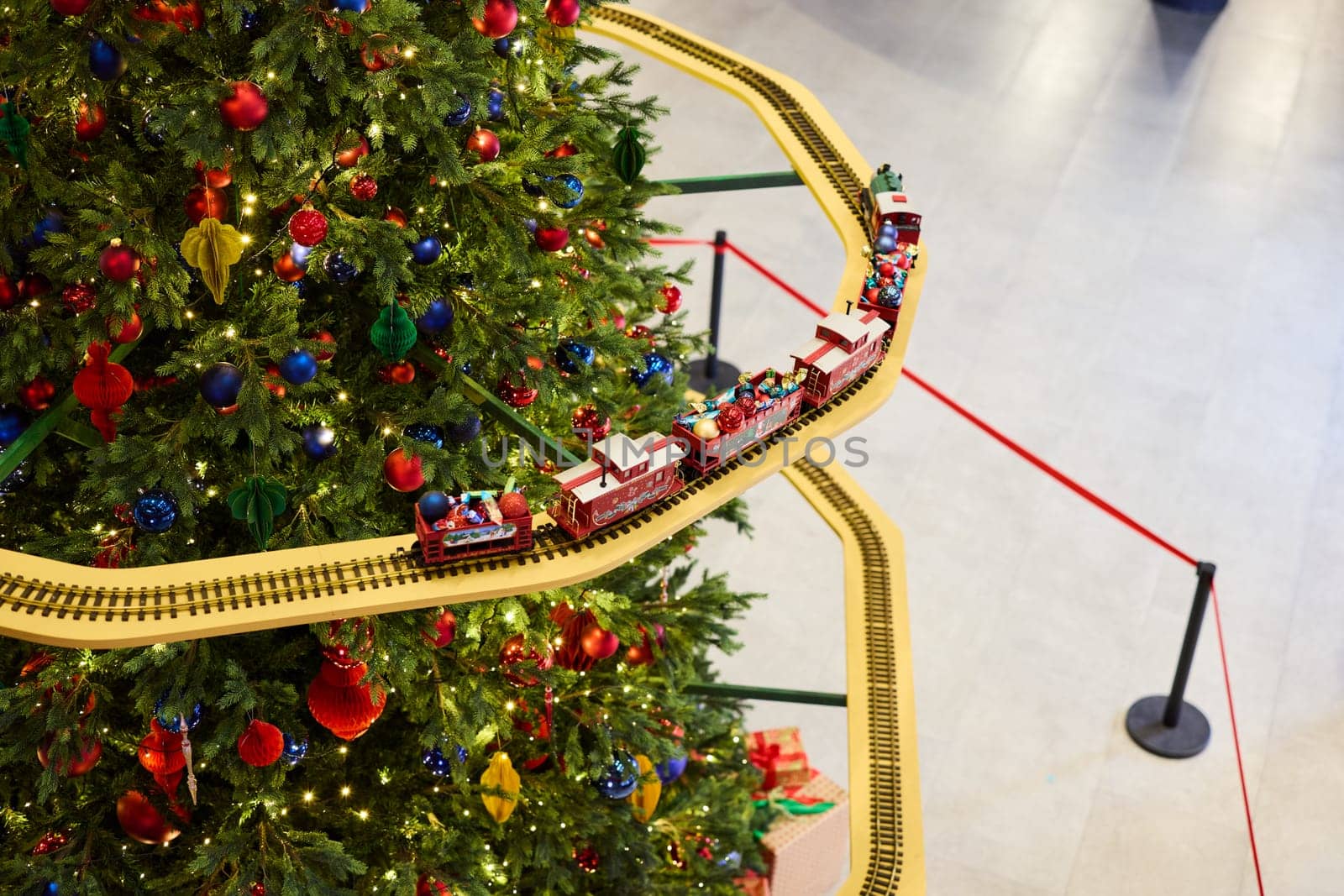 A vibrant and colorful train set is beautifully circling around a splendidly decorated Christmas tree, creating joy