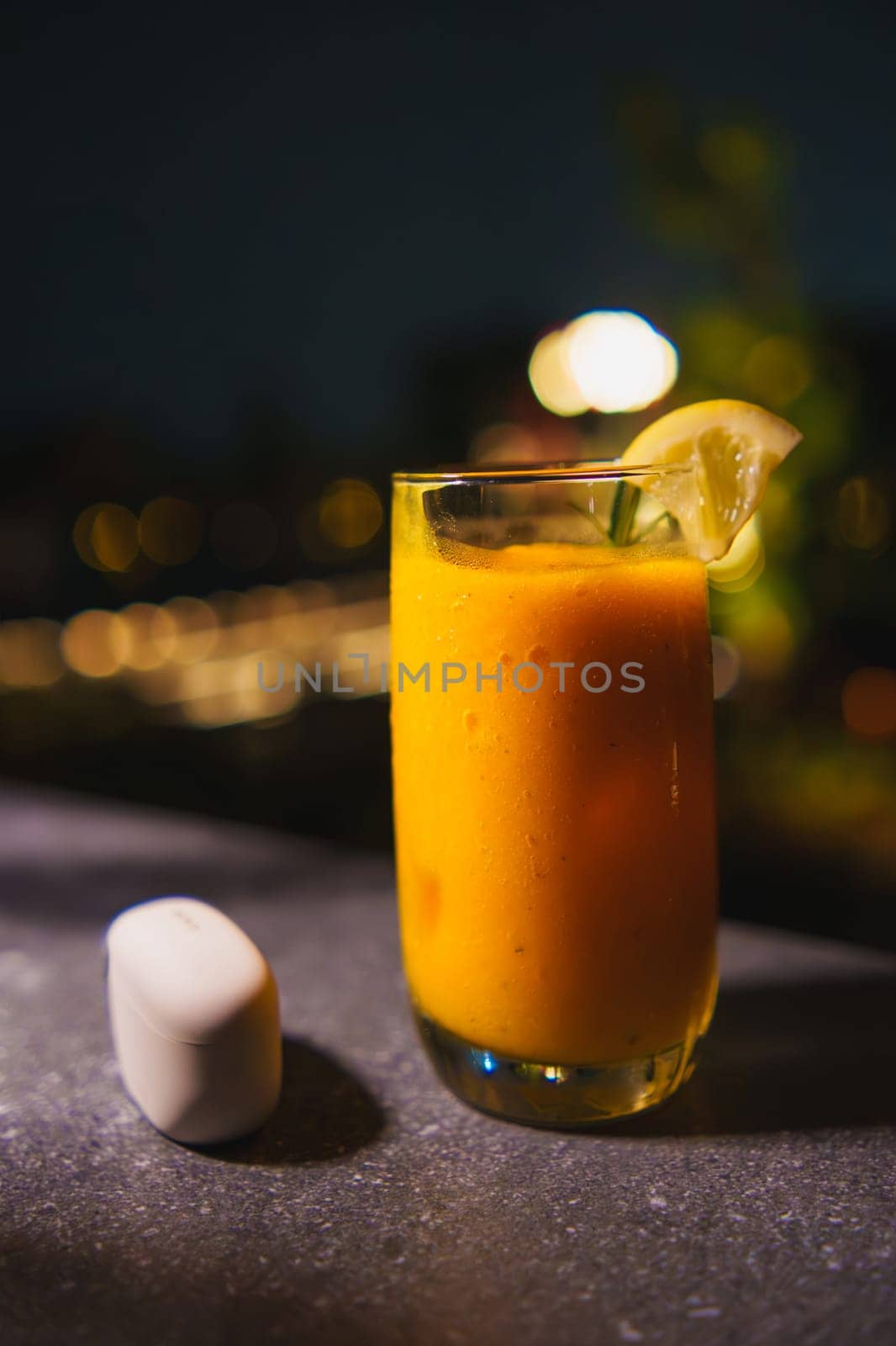 Refreshing mango smoothie with a lime garnish in a tall glass, served on a dark bar counter with bokeh lights in the background.