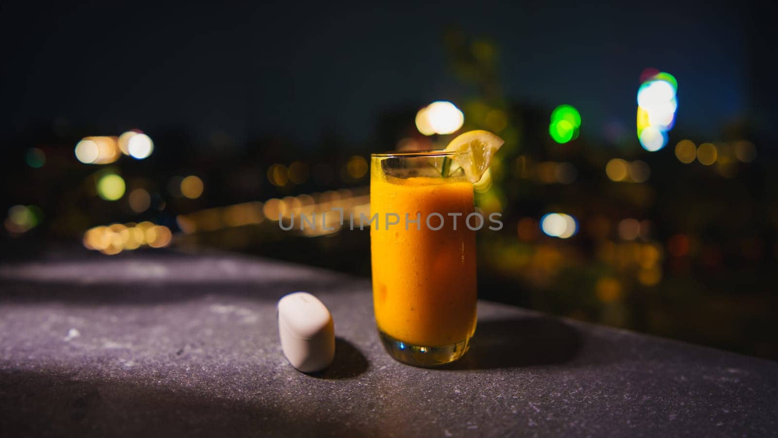 Glass of orange juice with a slice of lemon on a city night background.