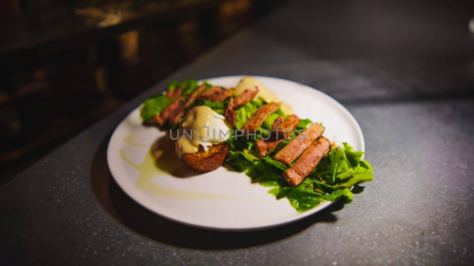 Gourmet steak on a bed of greens served on a white plate, with elegant dark background in the cafe