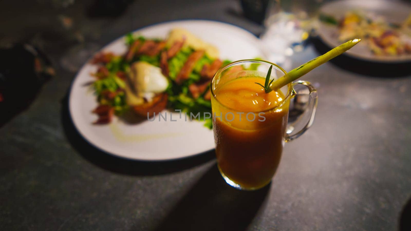 Glass of iced tea with straw, next to a plate of food on a dark table in the cafe