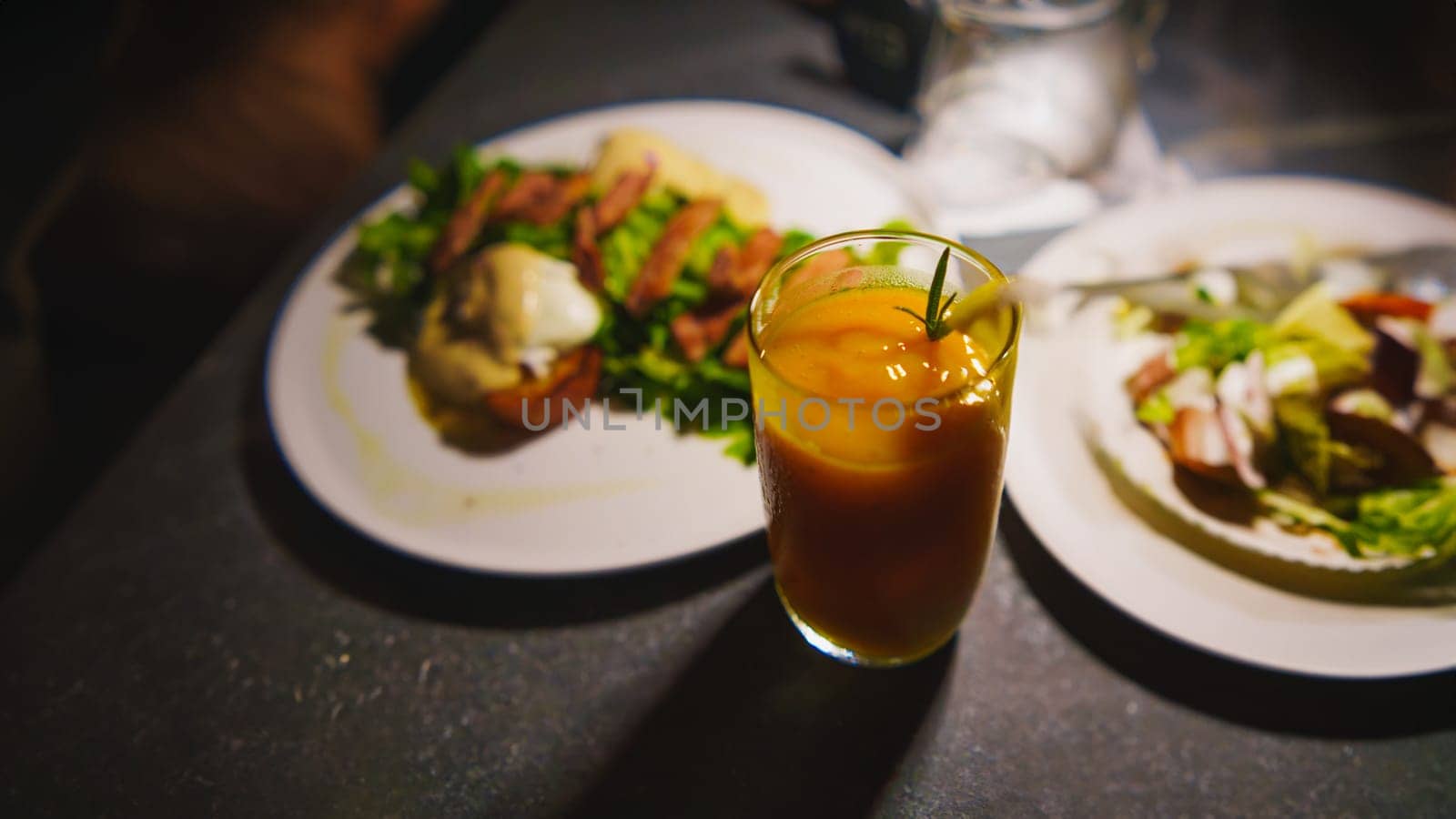 Elegant dining setting with a glass of orange drink and gourmet dishes in a dimly lit ambiance in the night