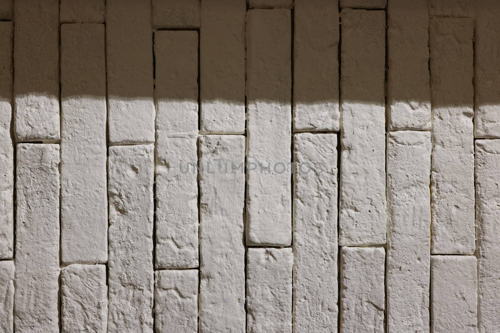 A closeup image of a textured white wall showcasing uneven brick patterns and soft, artistic shadows